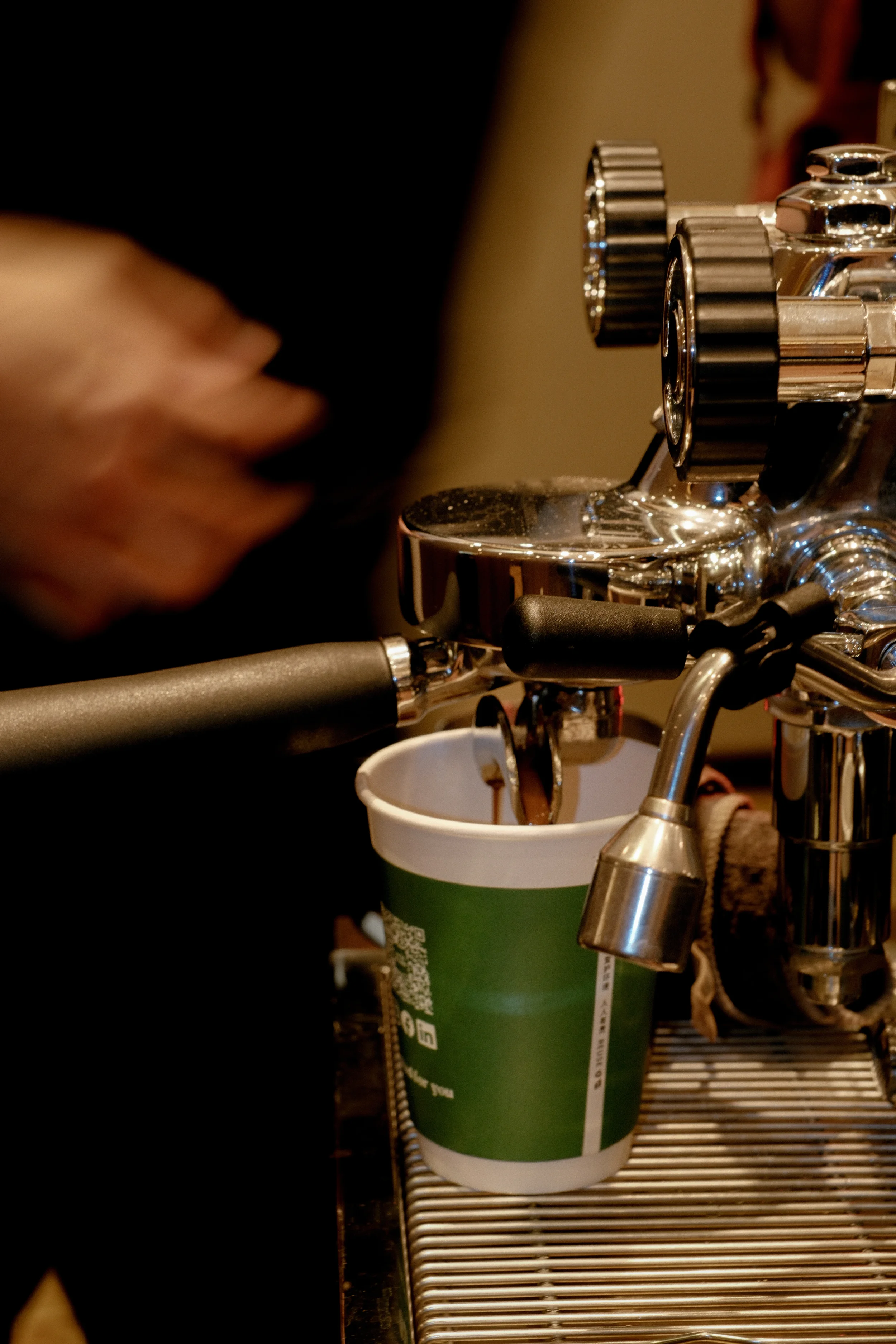 Close-up of a coffee espresso machine pouring coffee into a paper cup.