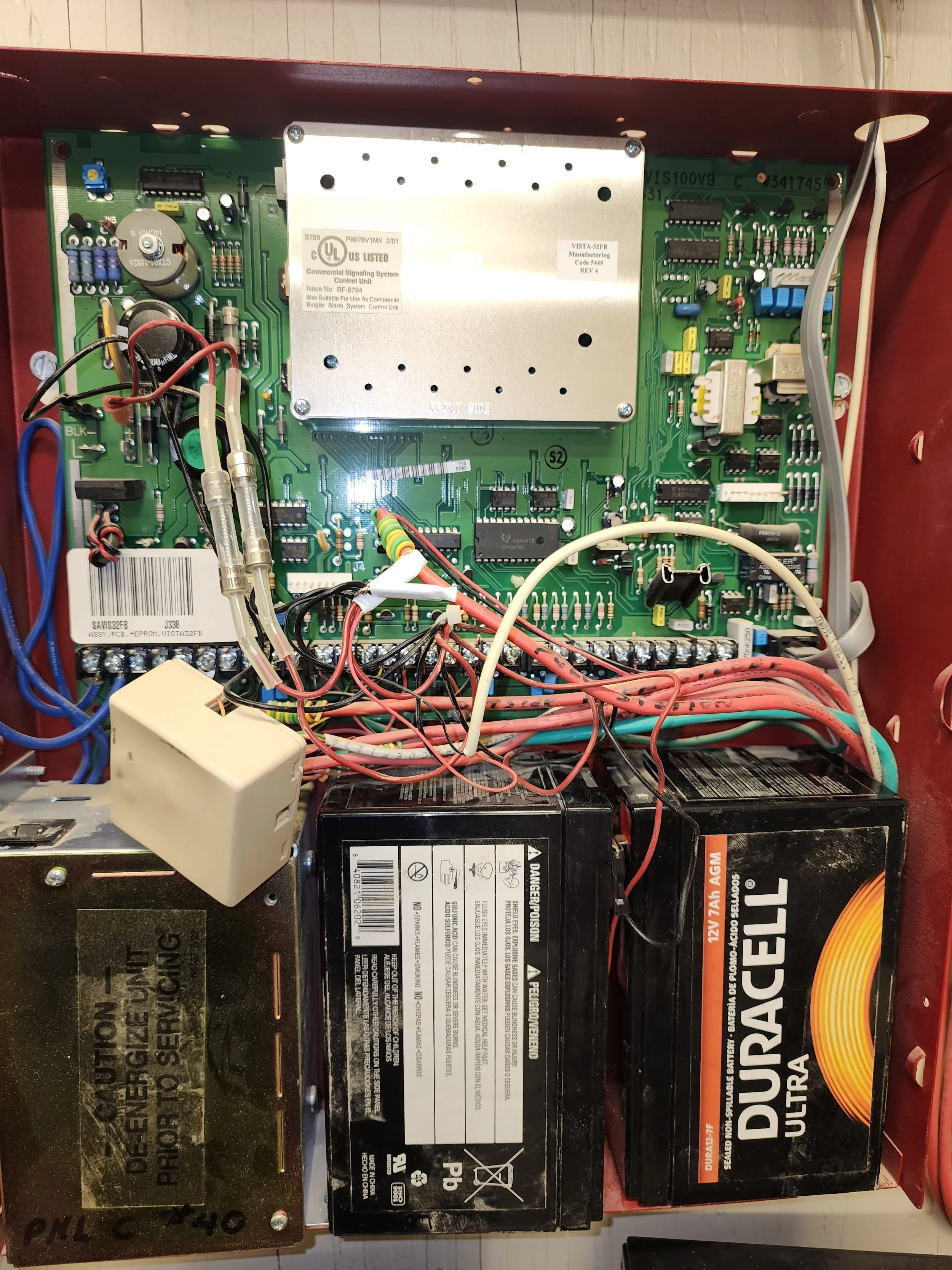 Inside of a mechanical control panel with circuit boards, wires, and batteries.