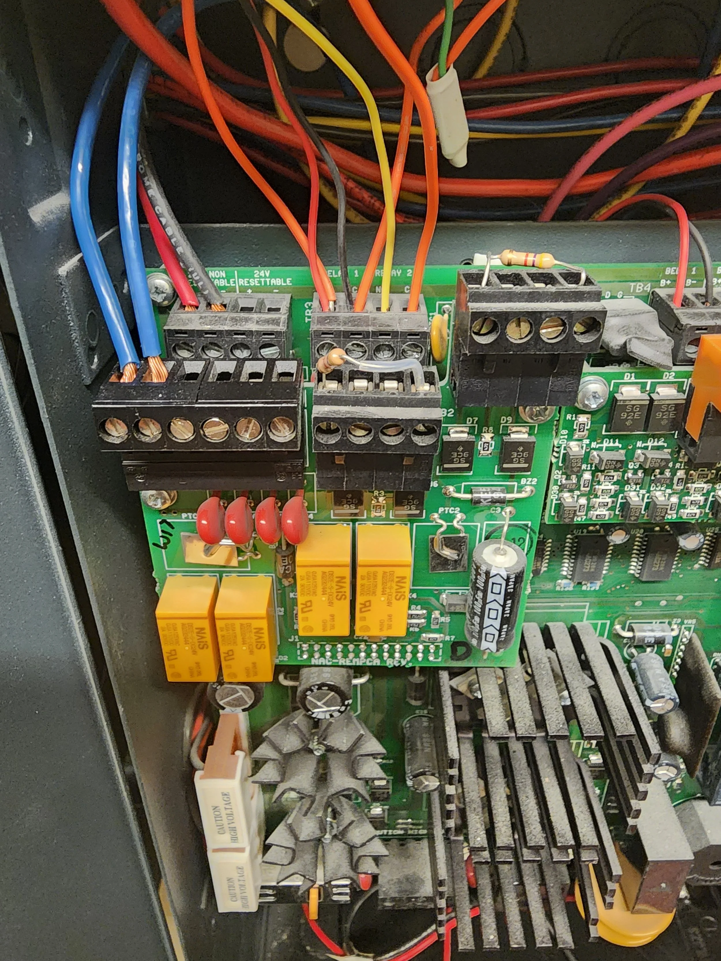 Close-up of an electronic circuit board inside a device, showing various wires, relays, resistors, capacitors, and heatsinks.