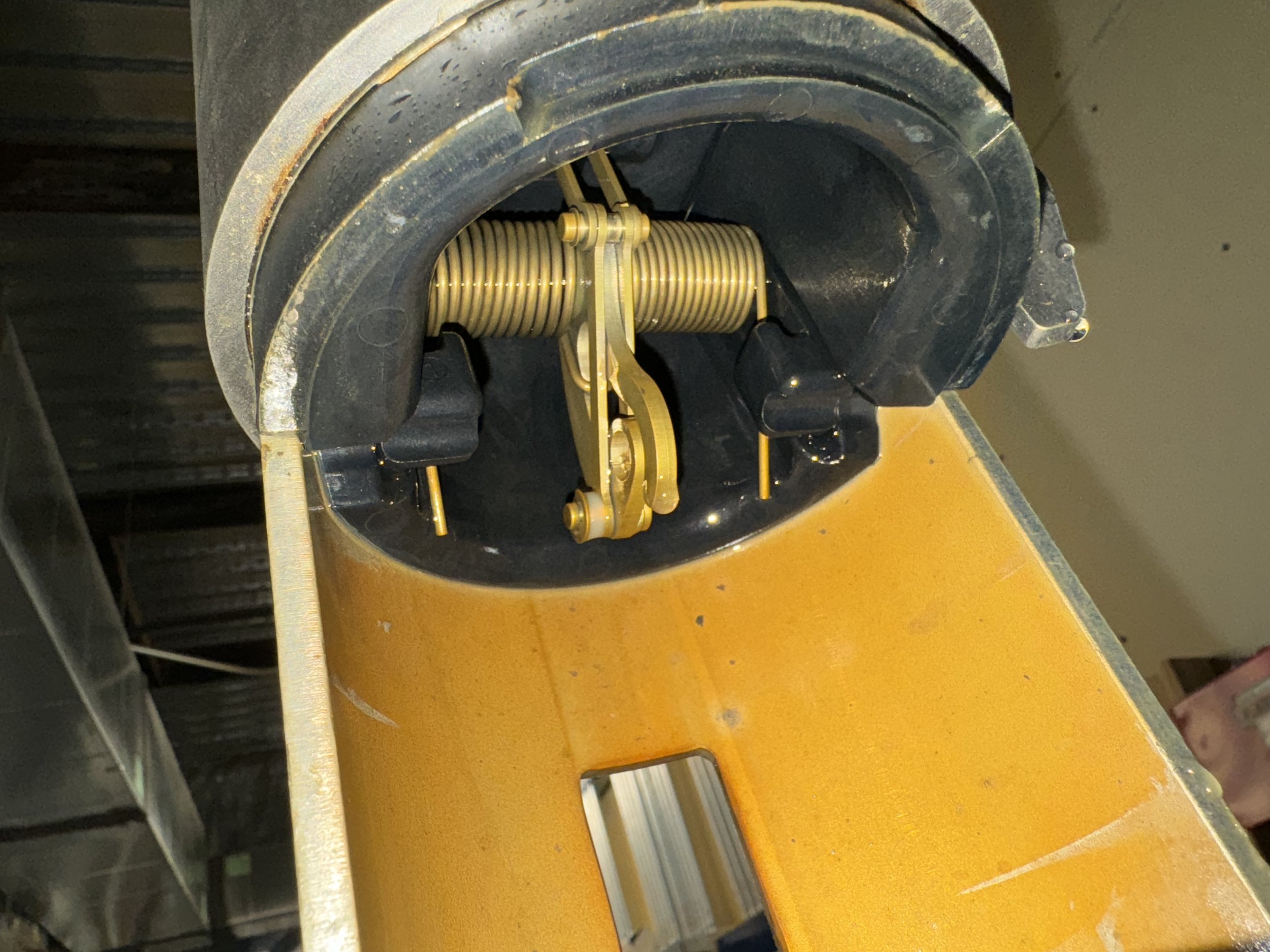 Close-up of a mechanical assembly with a gold-colored spring, a gold lever, and black components inside a black and yellow housing.