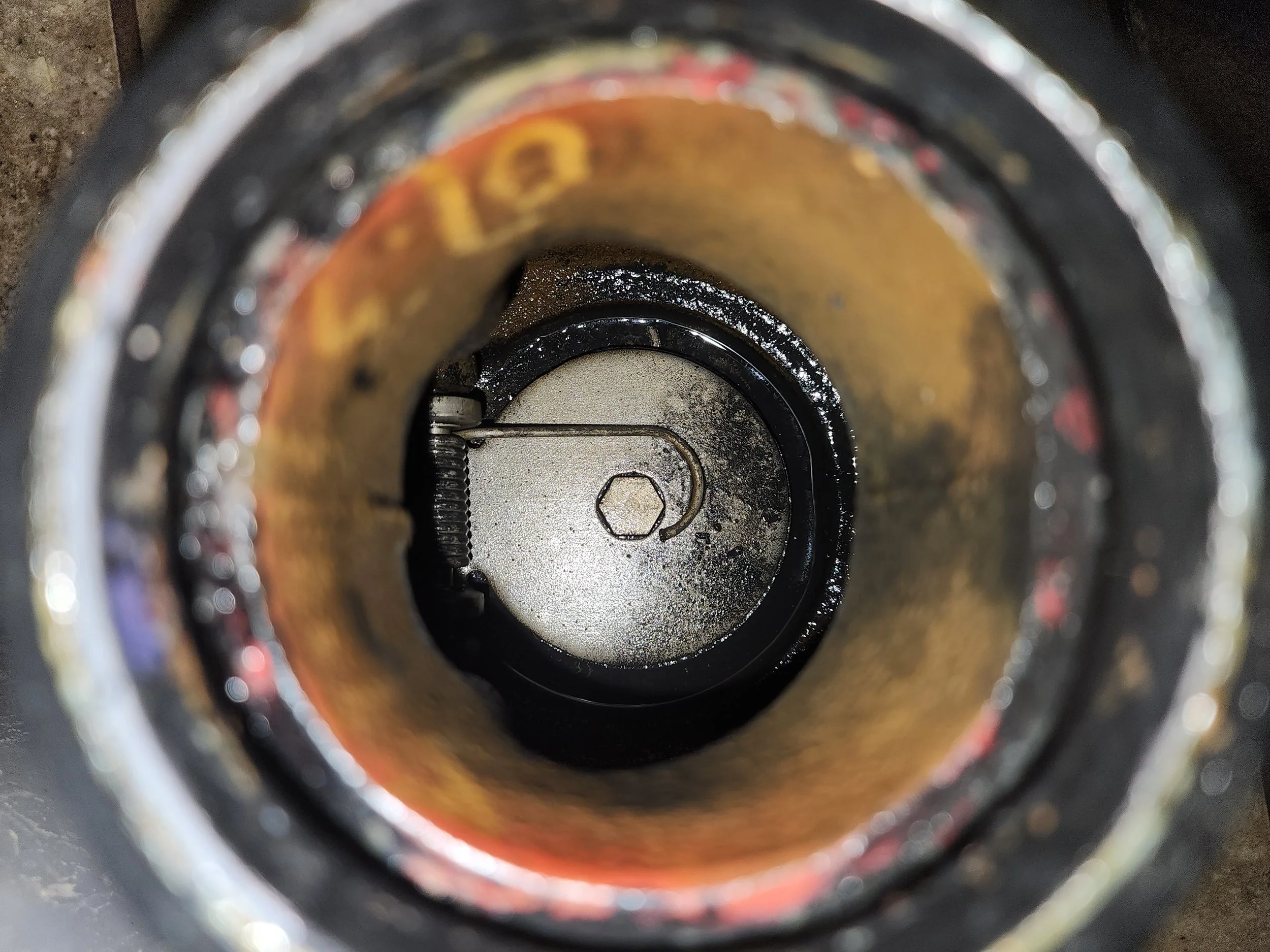 View of inside a mechanical or industrial component, showing a needle valve or similar device with a spring and a hex bolt.