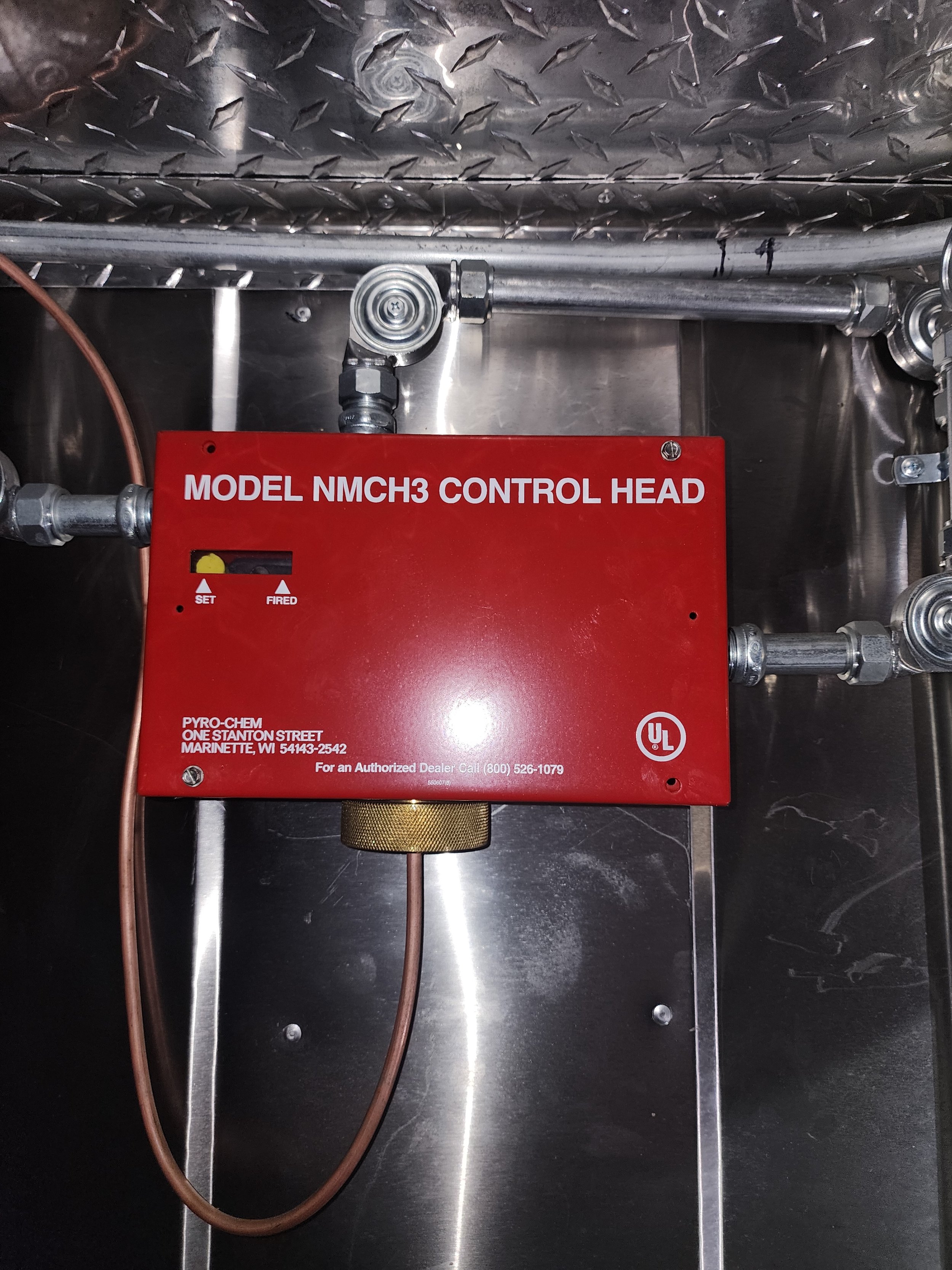 Red control head labeled 'Model NMCH3 Control Head' with wires and metal piping, mounted inside a stainless steel enclosure.
