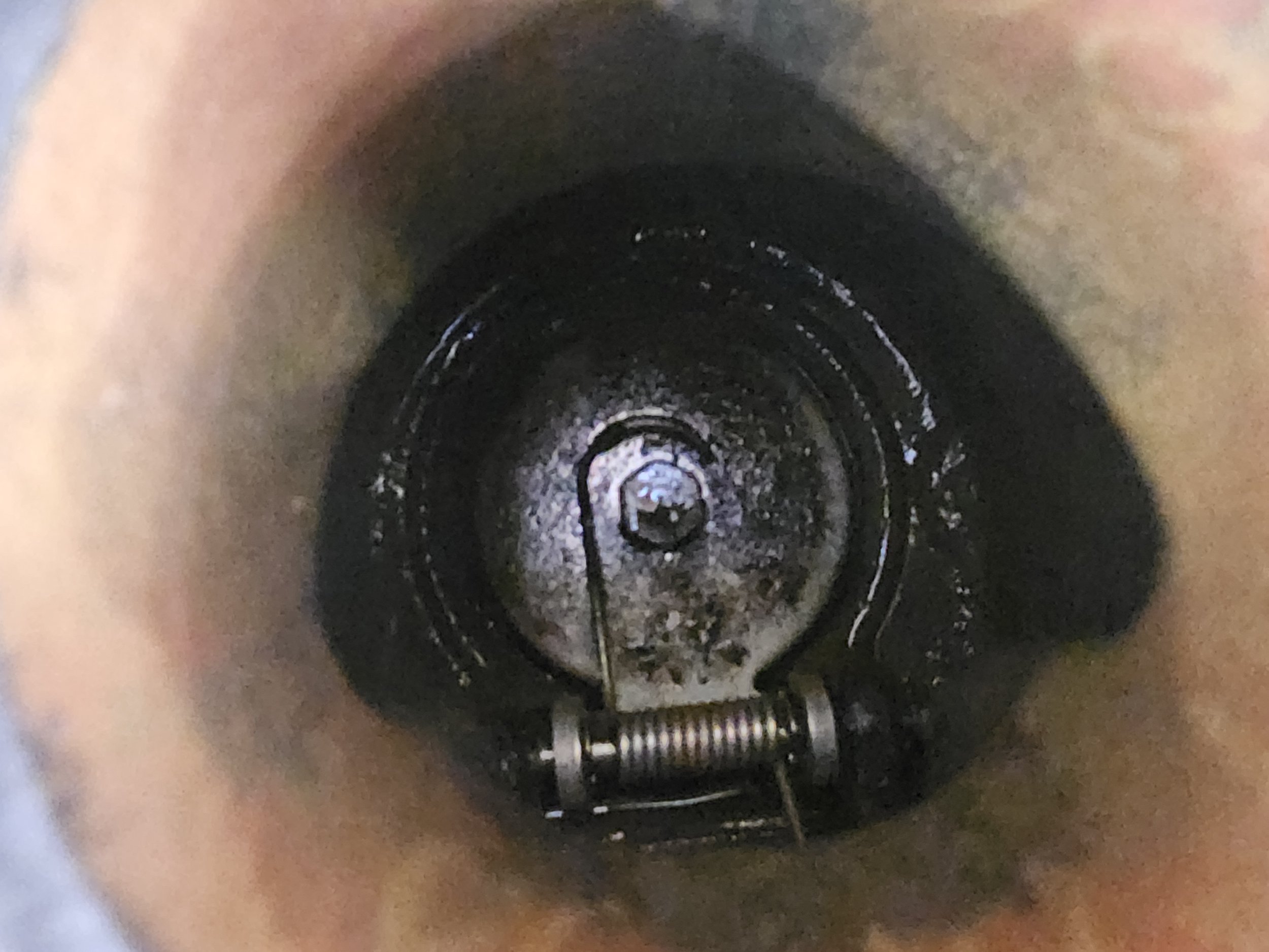 Close-up of the inside of a metal pipe or cylinder, showing a tense coil spring and a pin or rod, with some dirt or grime at the bottom.