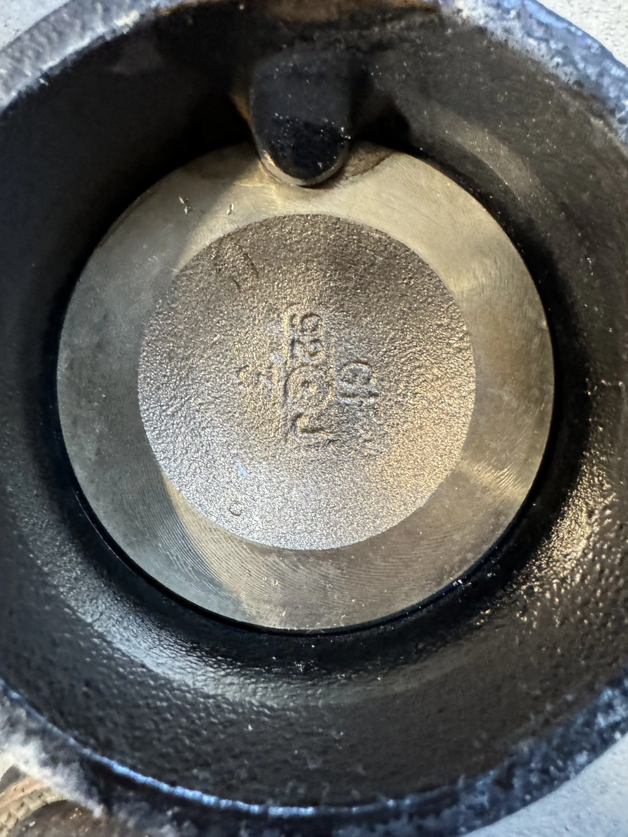 Close-up of the inside of a metal cylinder, possibly part of an engine or machinery, with stamped numbers and markings on the bottom surface.