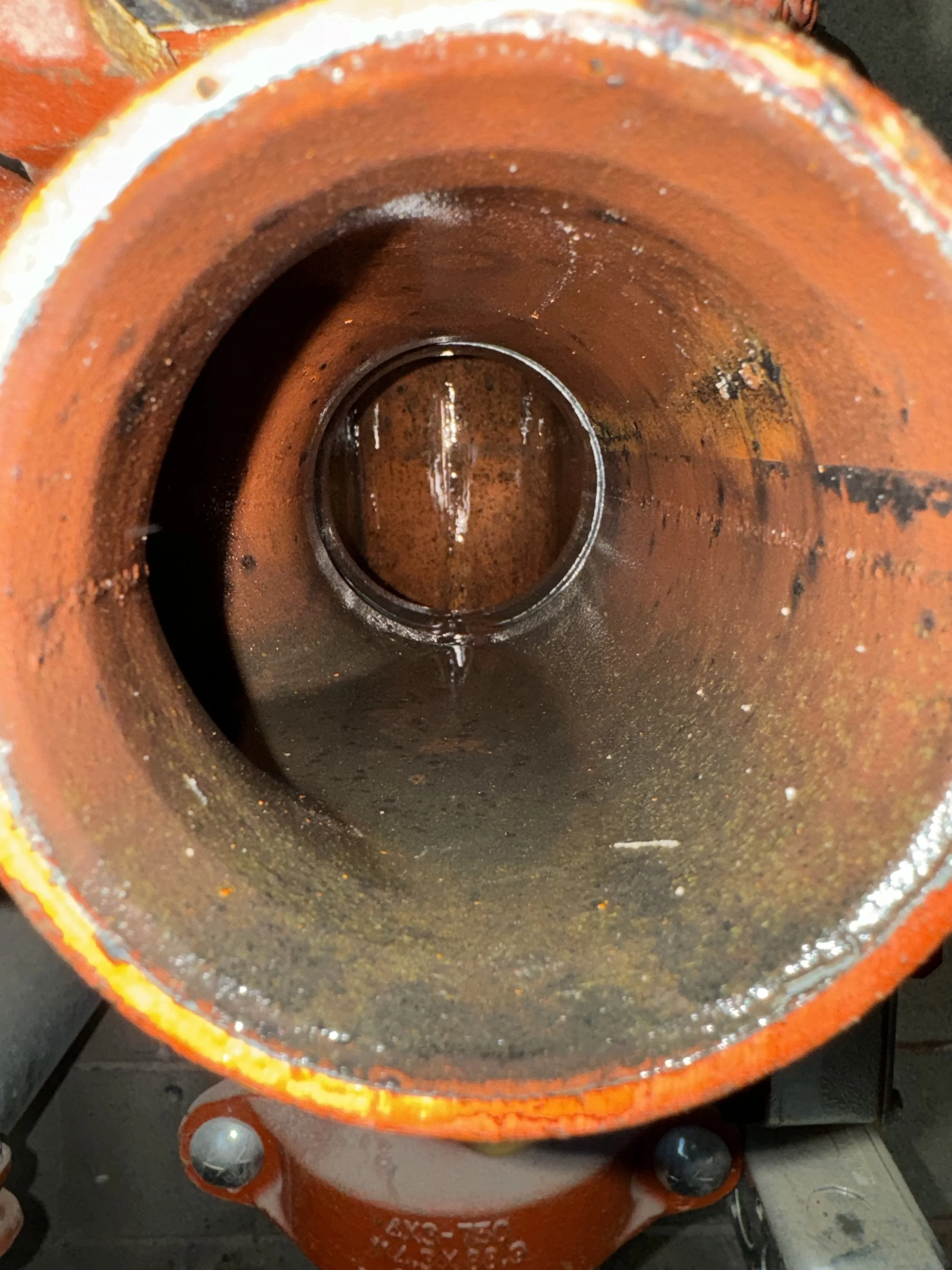 Inside view of a rusty orange metal pipe or cylinder with water at the bottom.