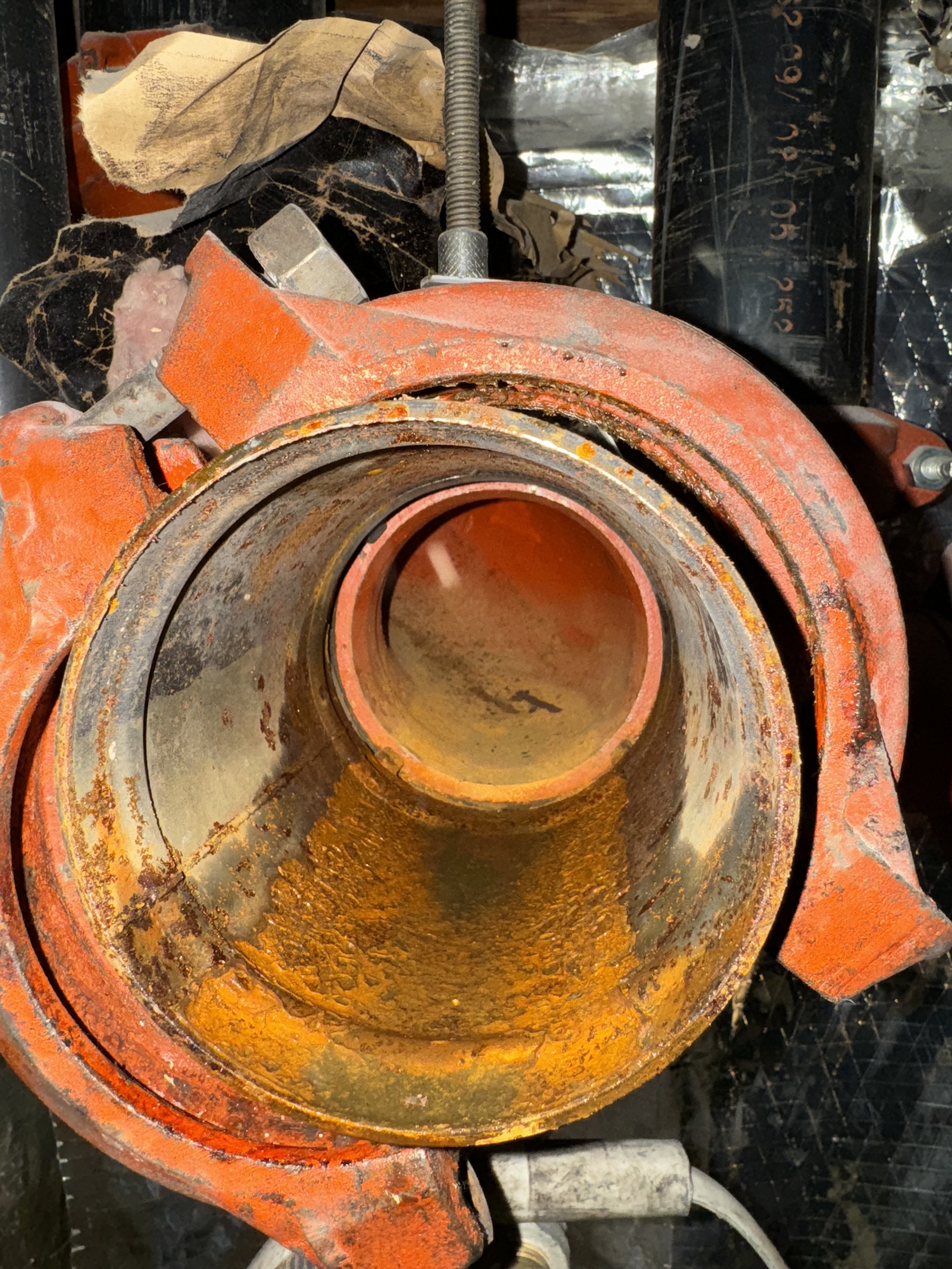Close-up of an orange, rusty mechanical part, possibly a pump or motor housing, with a large central cylindrical opening.