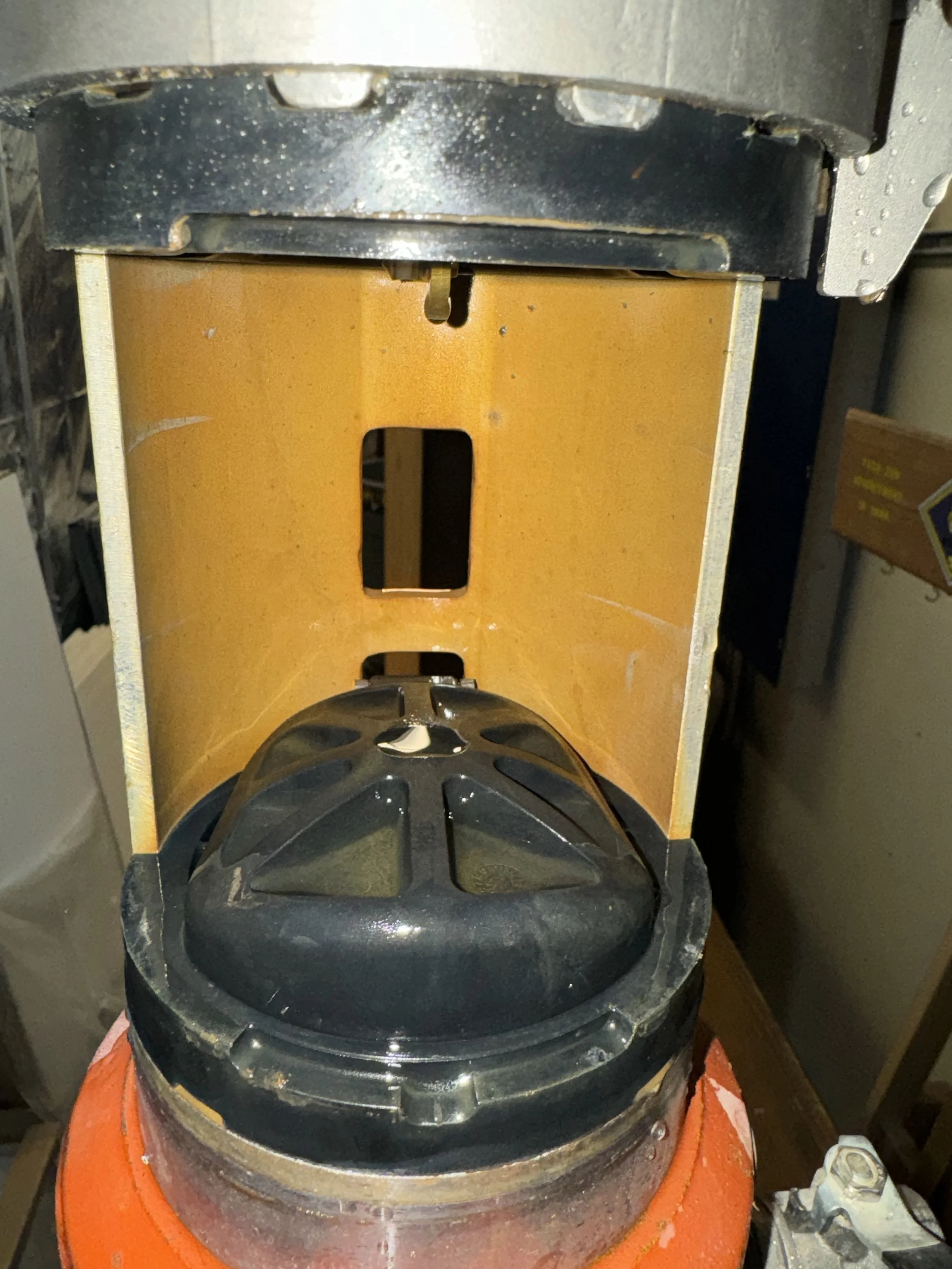 Close-up of a black safety helmet inside an orange container, with a yellow protective shield behind.