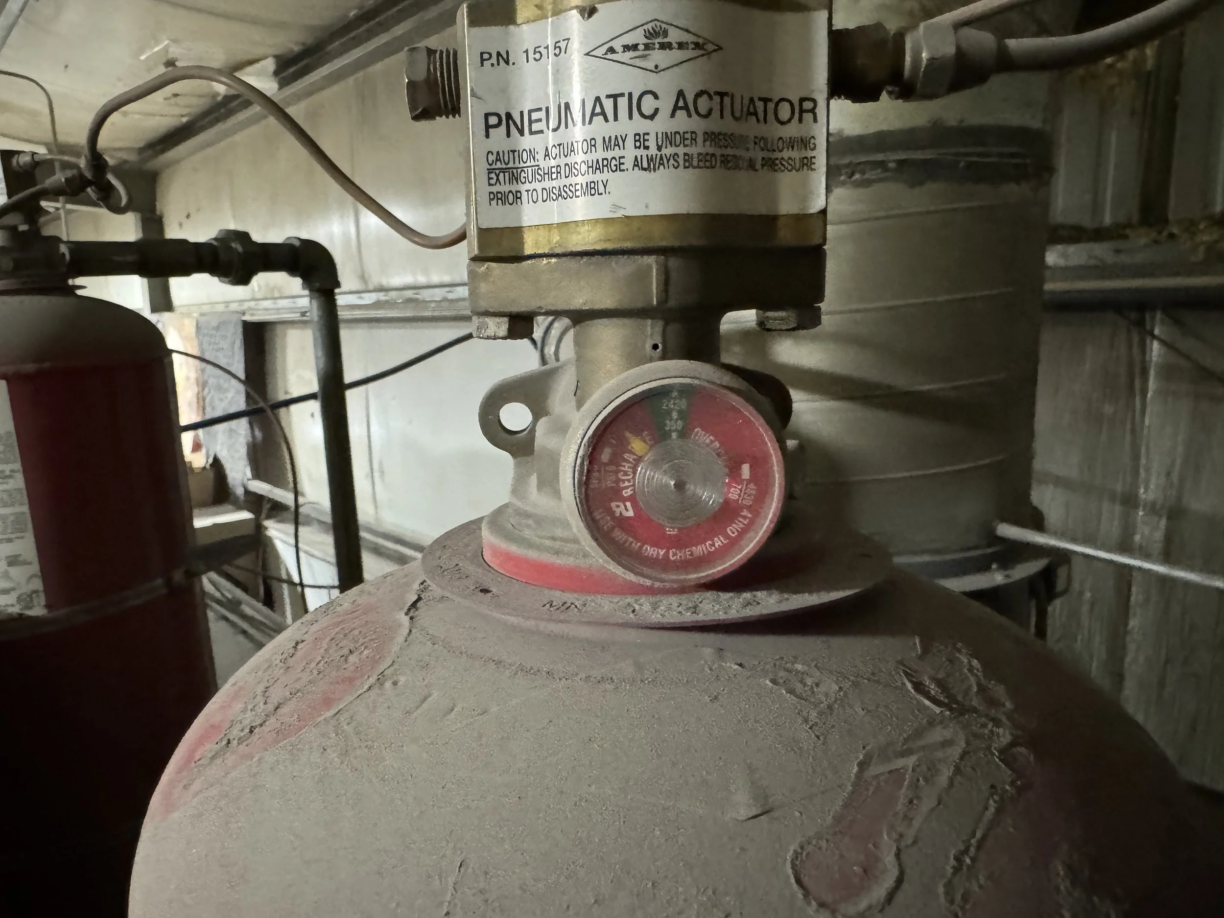 Close-up of a dusty pneumatic actuator with a pressure gauge showing pressure level, mounted on a large industrial tank in a factory setting.