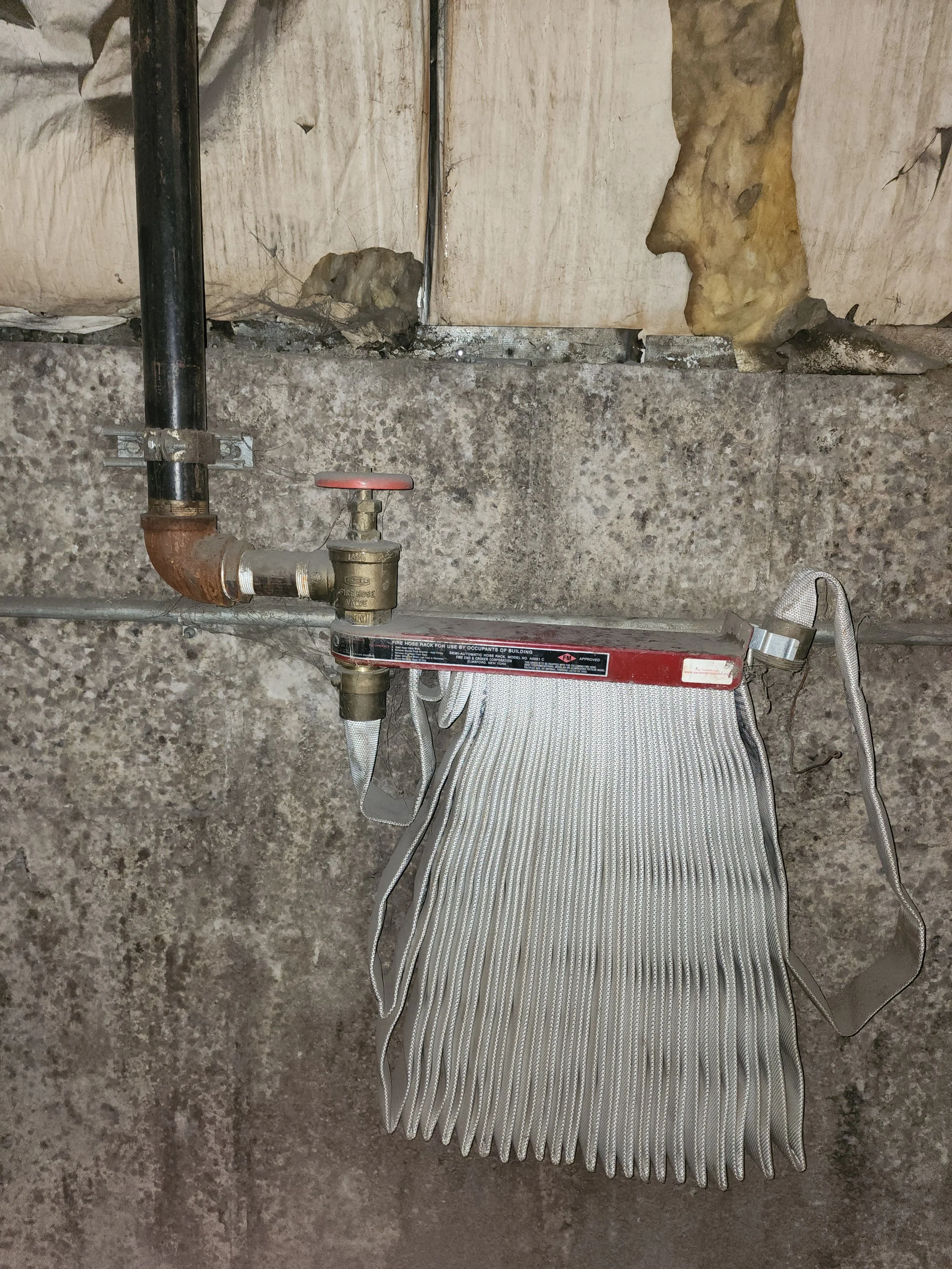 A fire sprinkler testing bag attached to a pipe with insulation and concrete wall background.