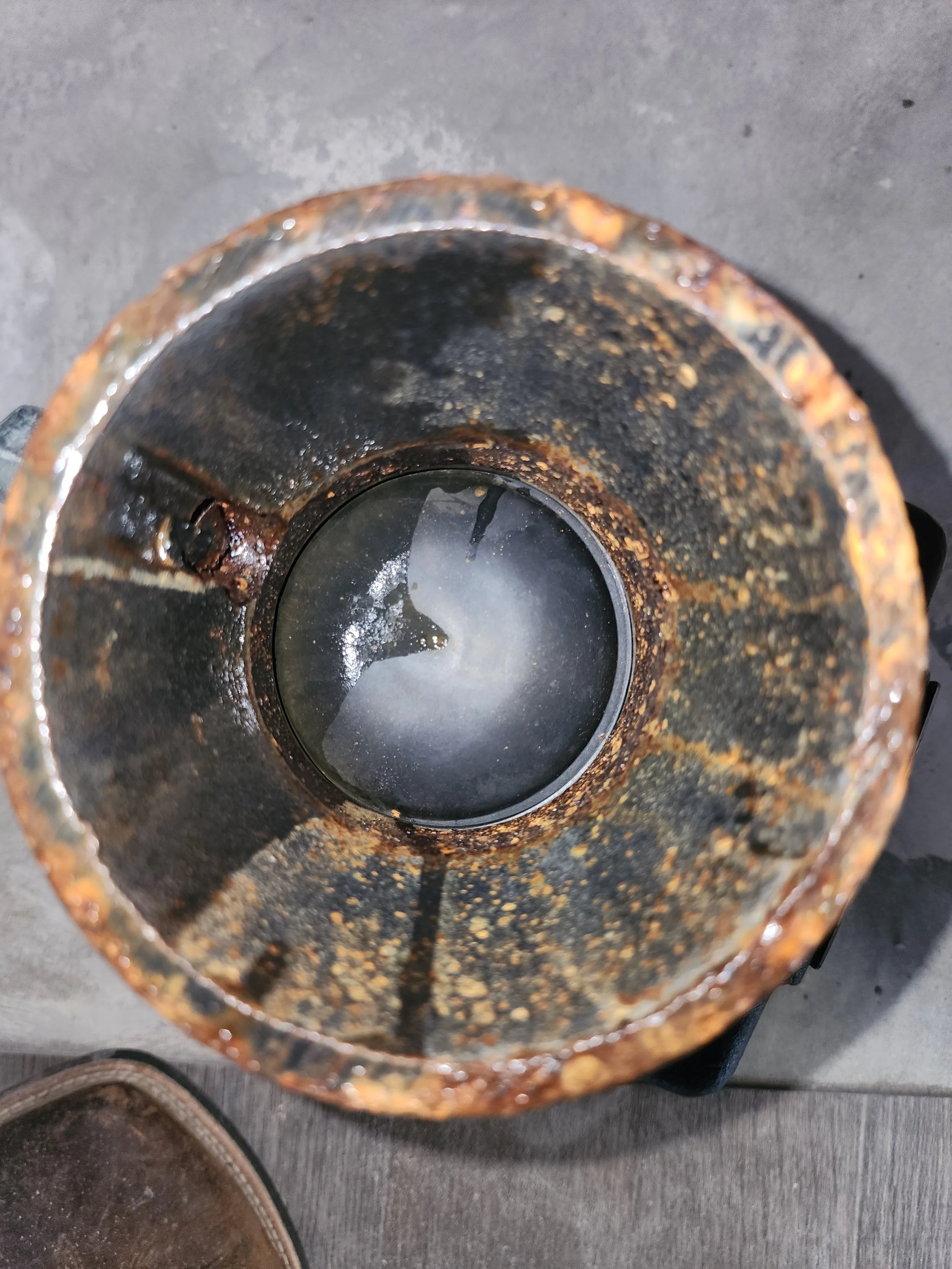 Top view of a rusty, corroded metal pipe with water inside.