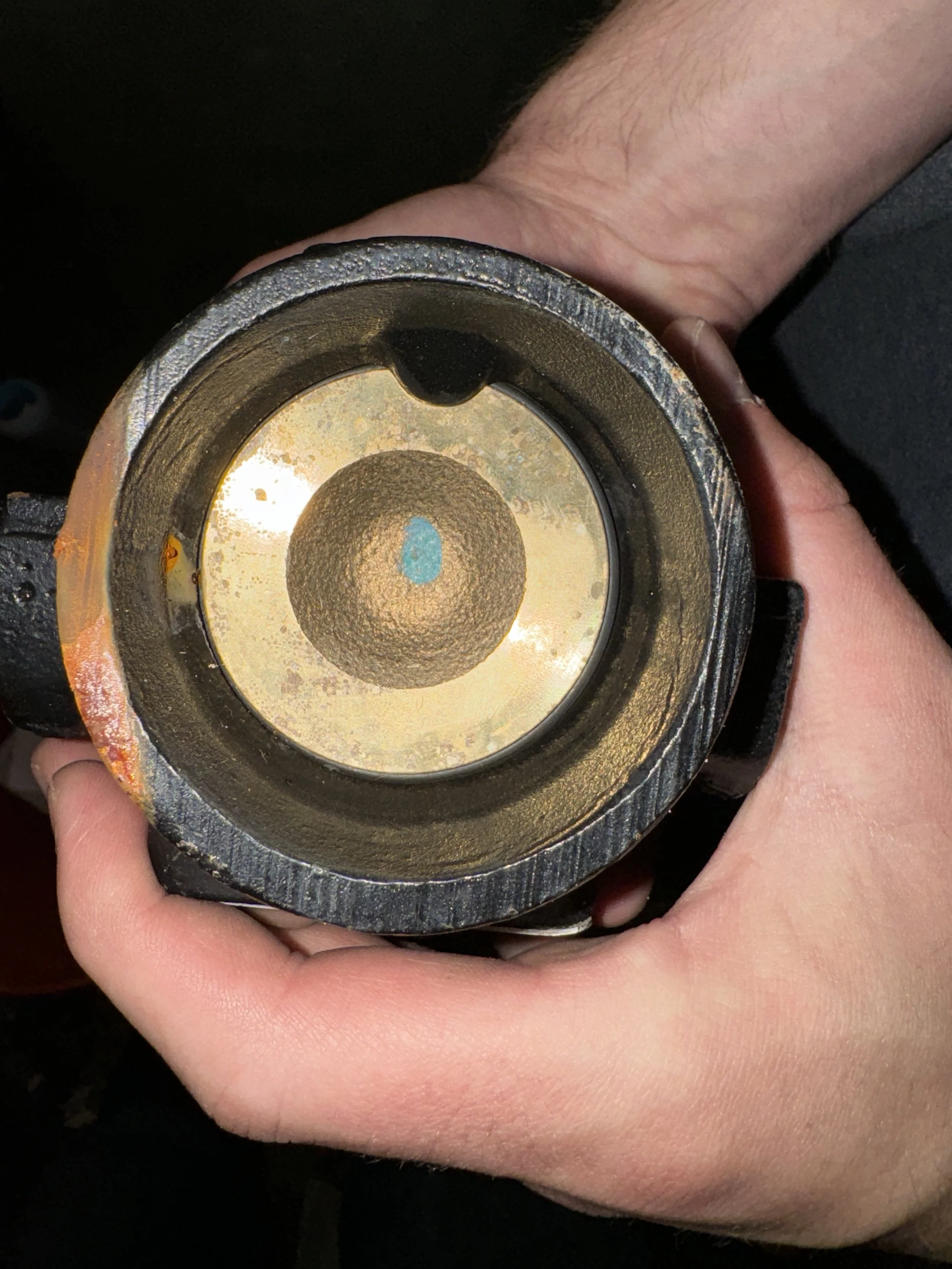 Close-up of a person's hand holding a metallic cylindrical object, possibly a mechanical part or tool, with a reflective interior surface.