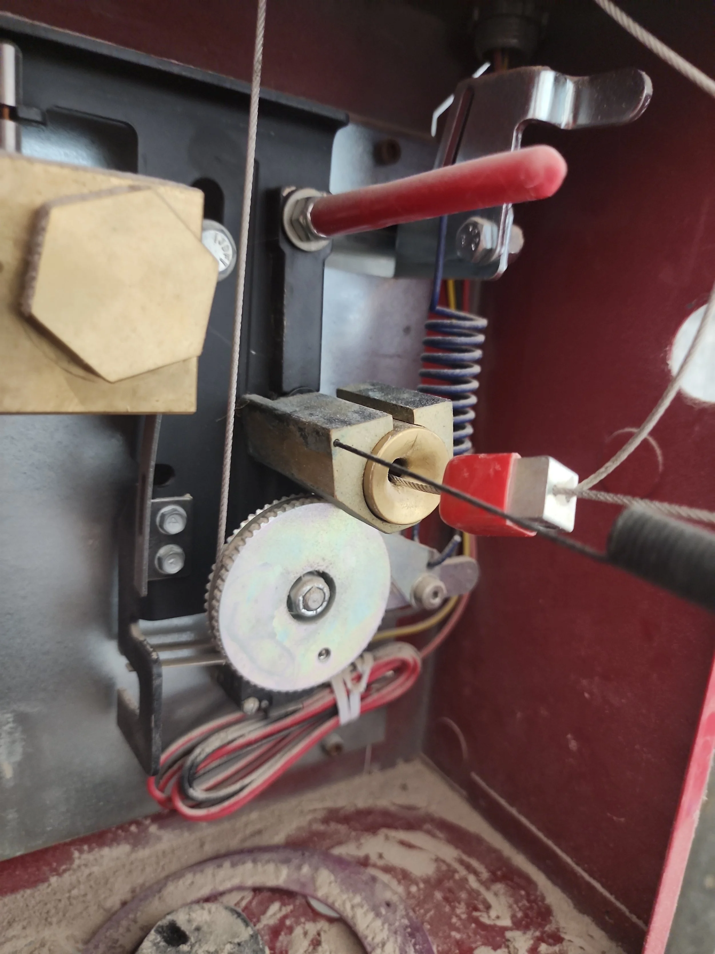 Close-up of mechanical components inside an old machine, including gears, a red handle, wires, and various metal parts.
