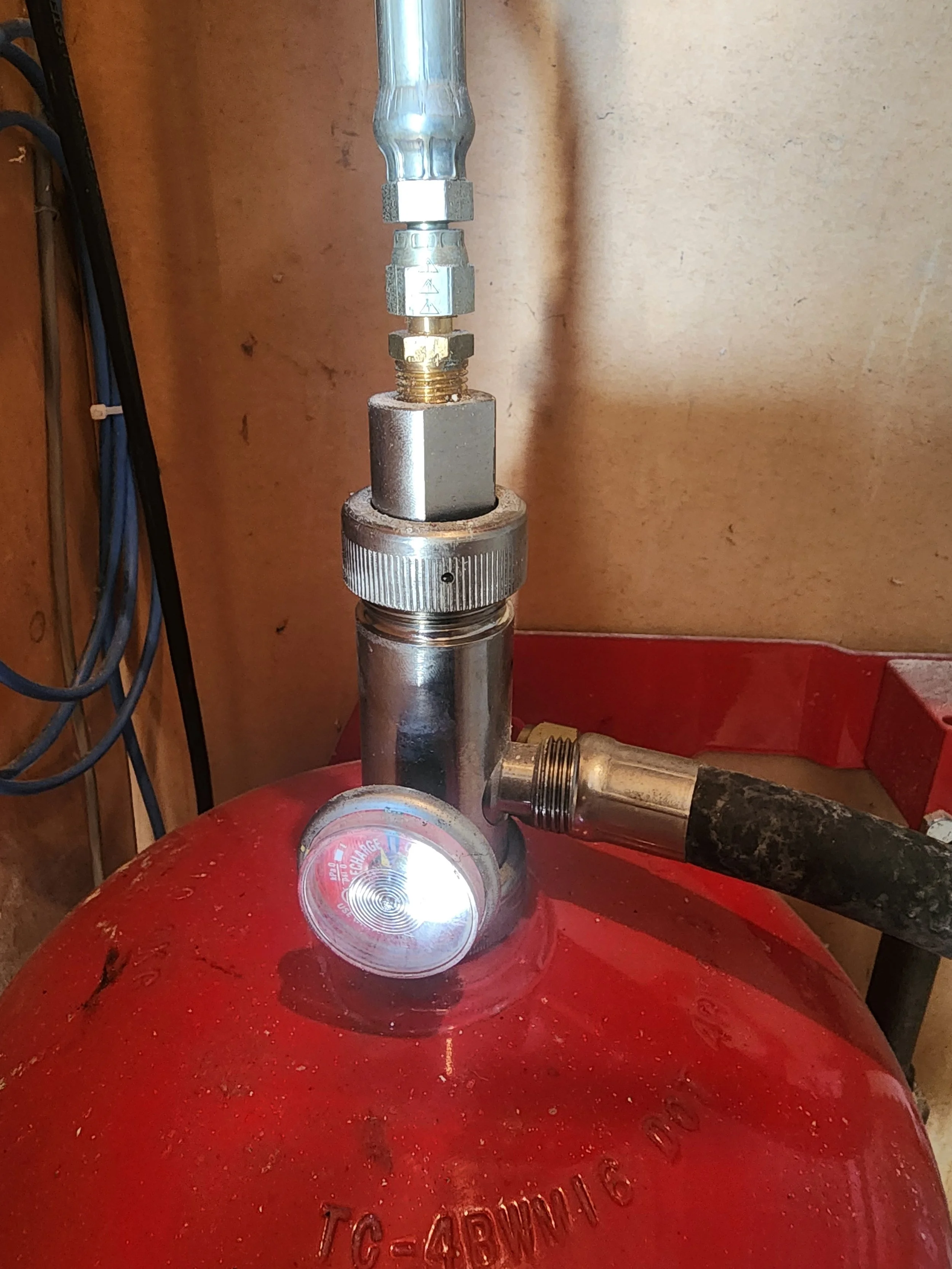 Close-up of a fire sprinkler head attached to a red fire suppression system tank, with metal pipes and fittings.