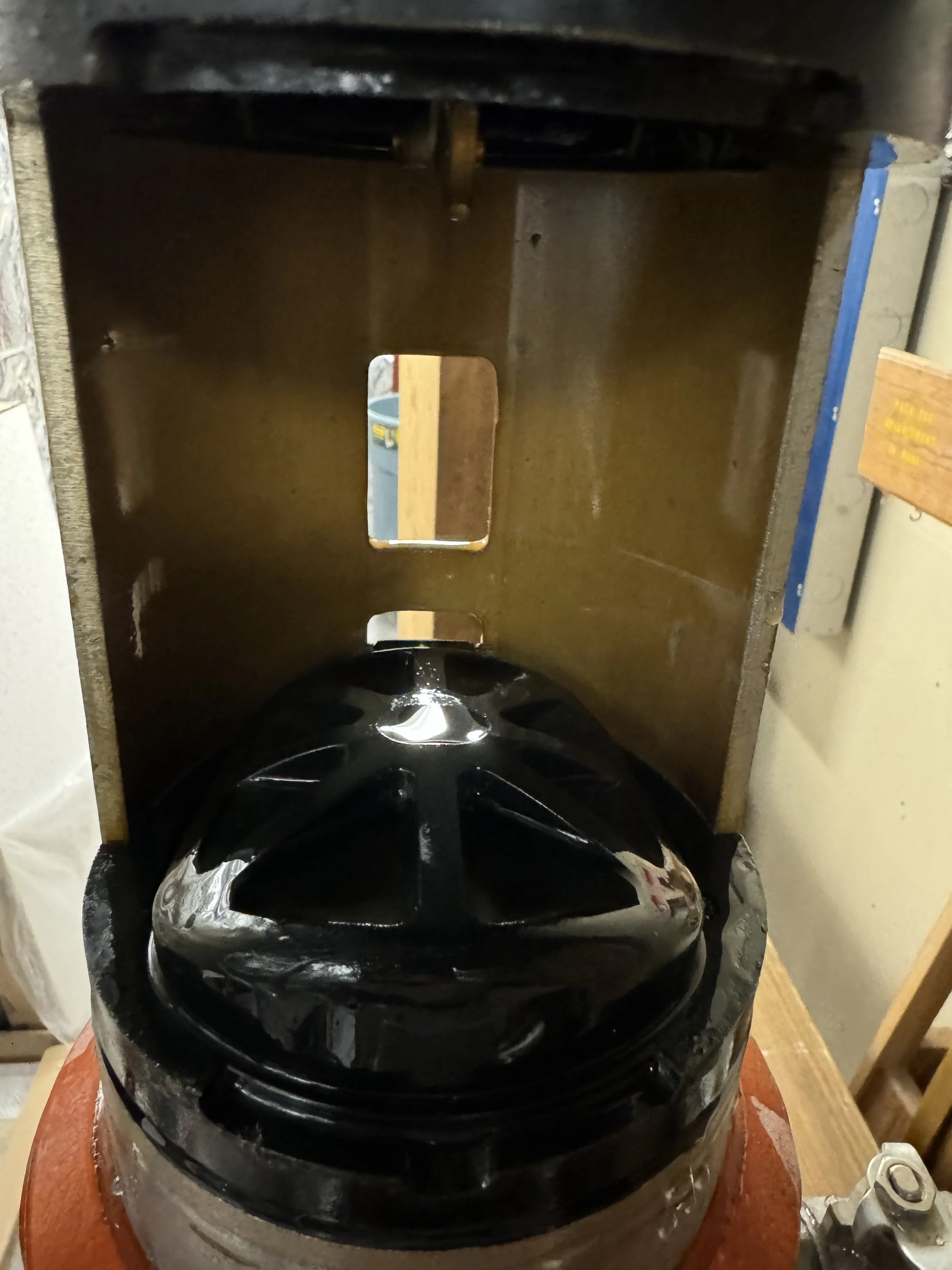 A black helmet placed inside a metallic sanding or polishing machine, with a metal shield or cover behind it.