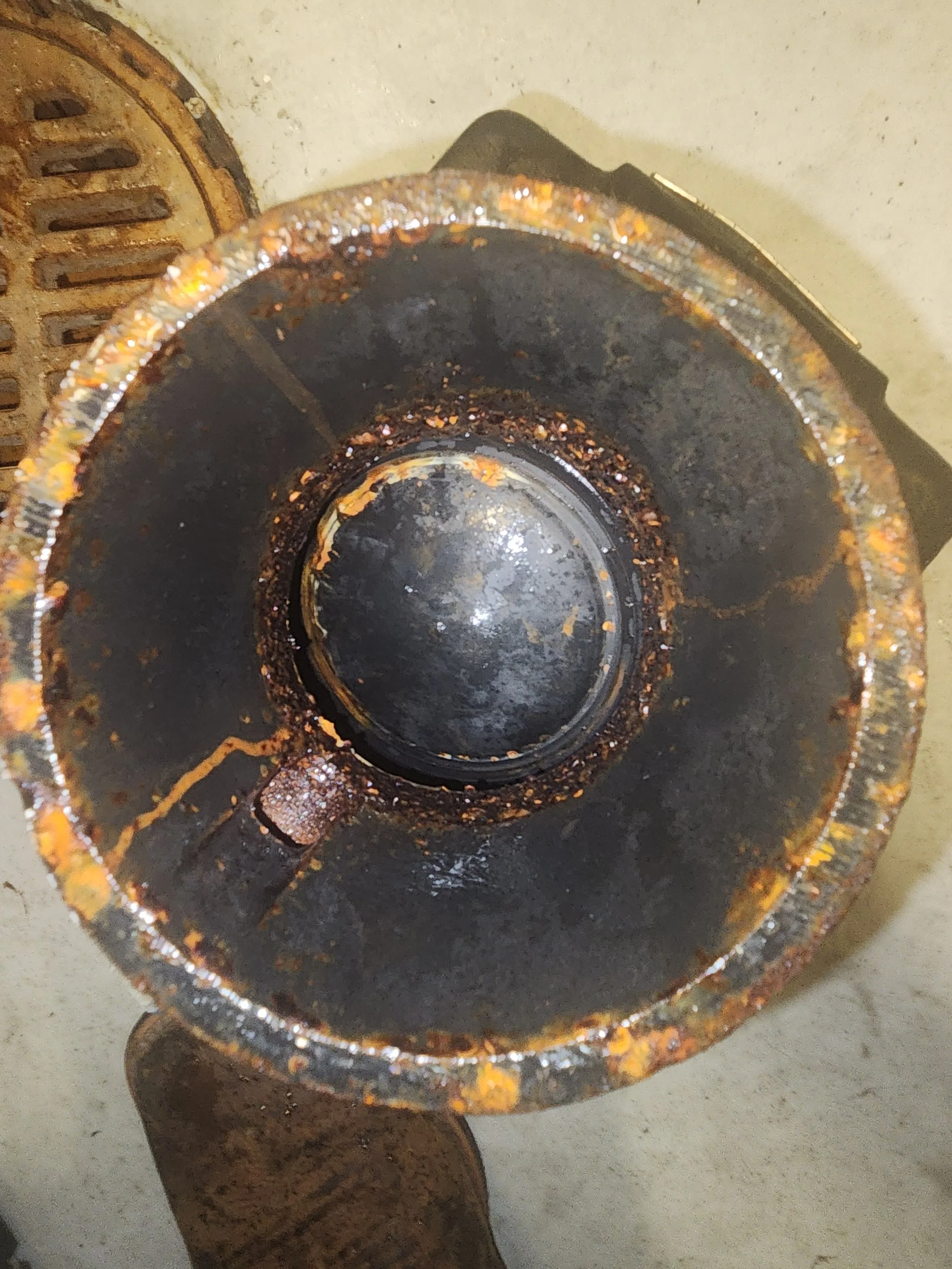Top view of a rusty, greasy metal pipe or cylindrical component, showing signs of corrosion and debris inside.