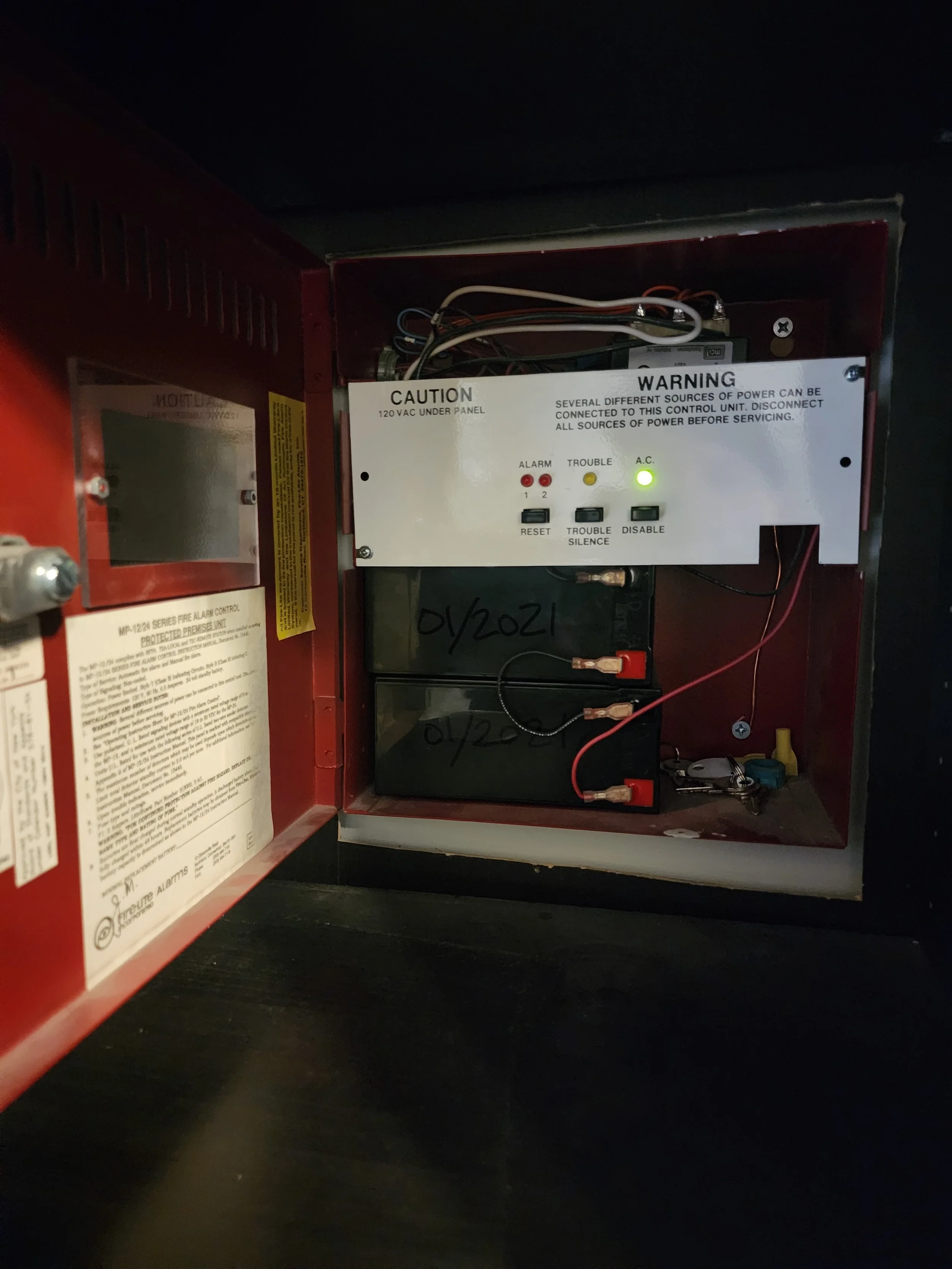 Open fire alarm control panel with wiring and indicator lights, including an alarm, trouble, and A.C. status lights inside a red metal box.