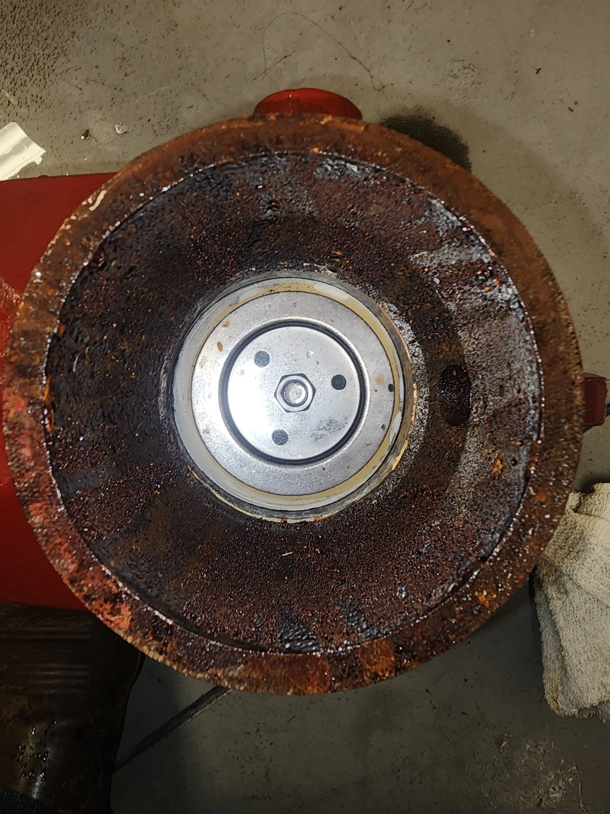Rusty circular metal component with a silver central part, resting on a concrete floor with a white cloth nearby.