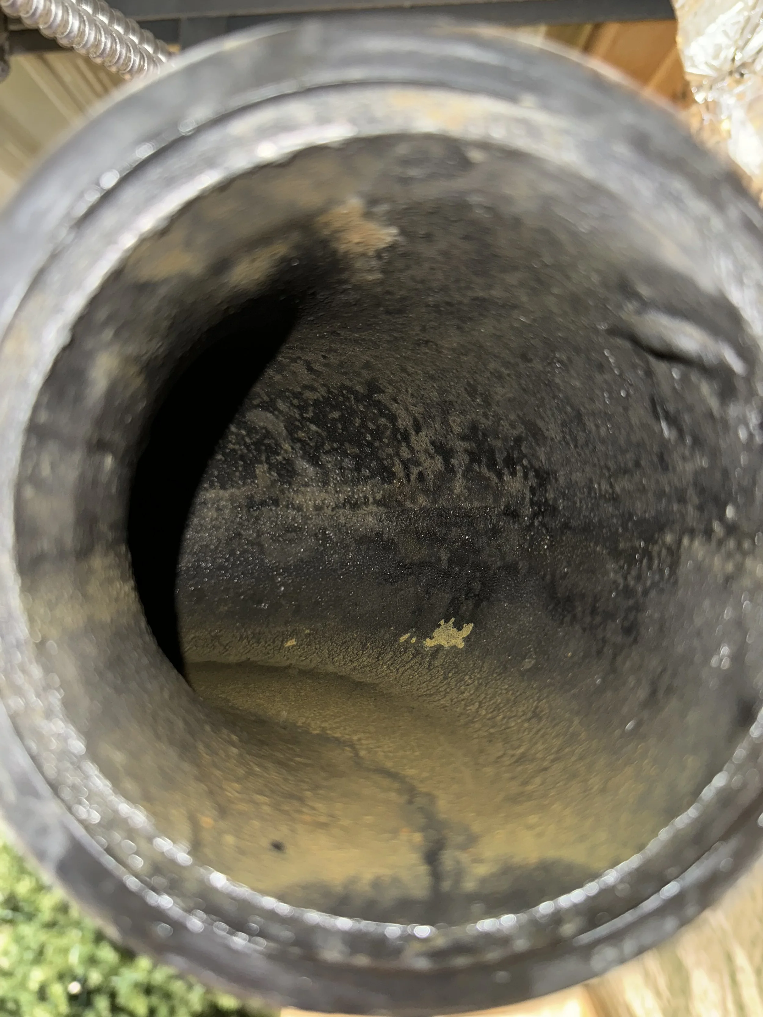 The interior of a dirty, greasy metal pipe with black soot and grime coating the inside surface.