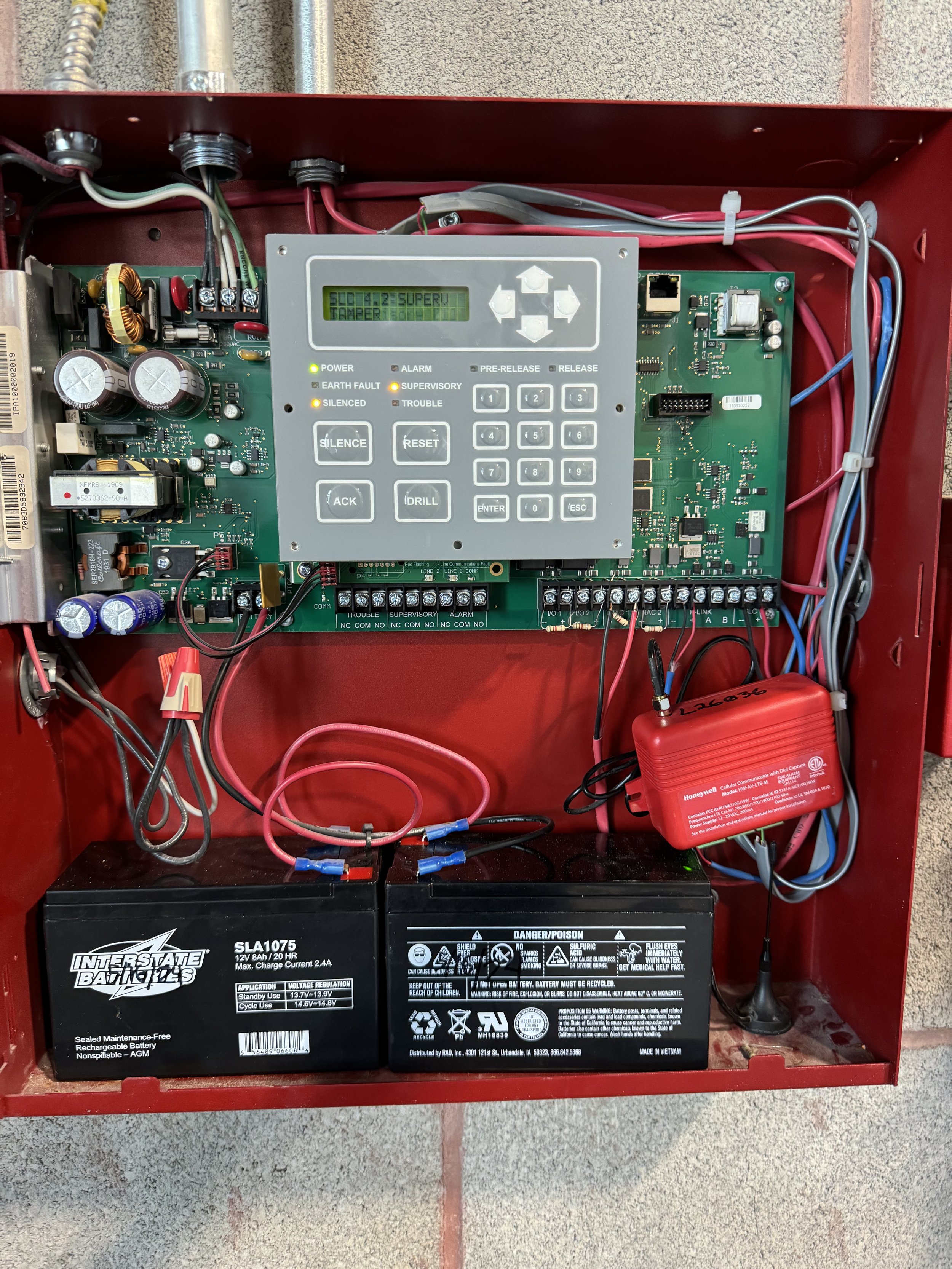 Interior of an alarm system box with batteries, circuit boards, wires, and a control panel with a display and keypad.