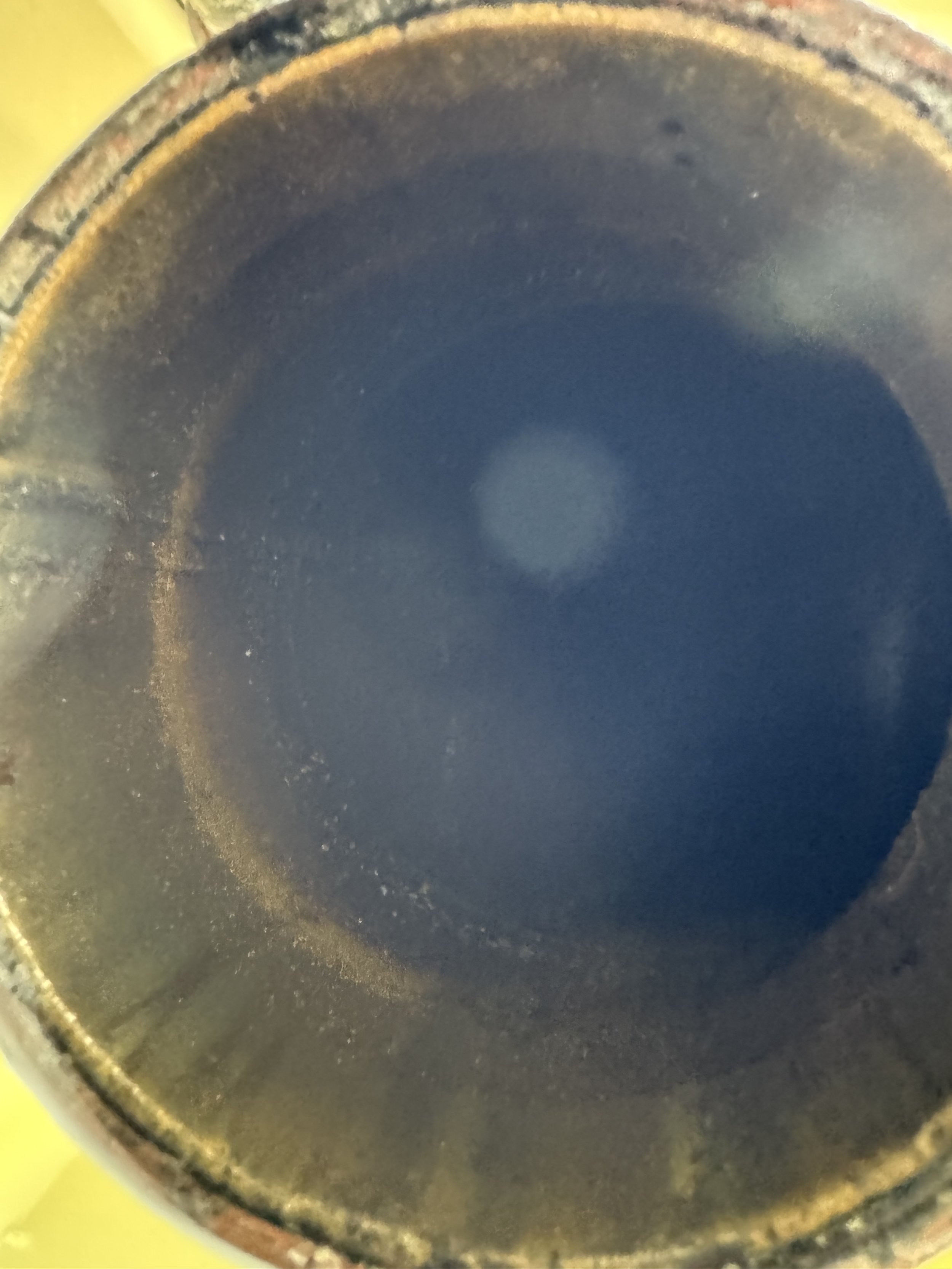 Close-up of the inside of a blackened, rusty metal container or pipe with some residue or debris along the inner edge.