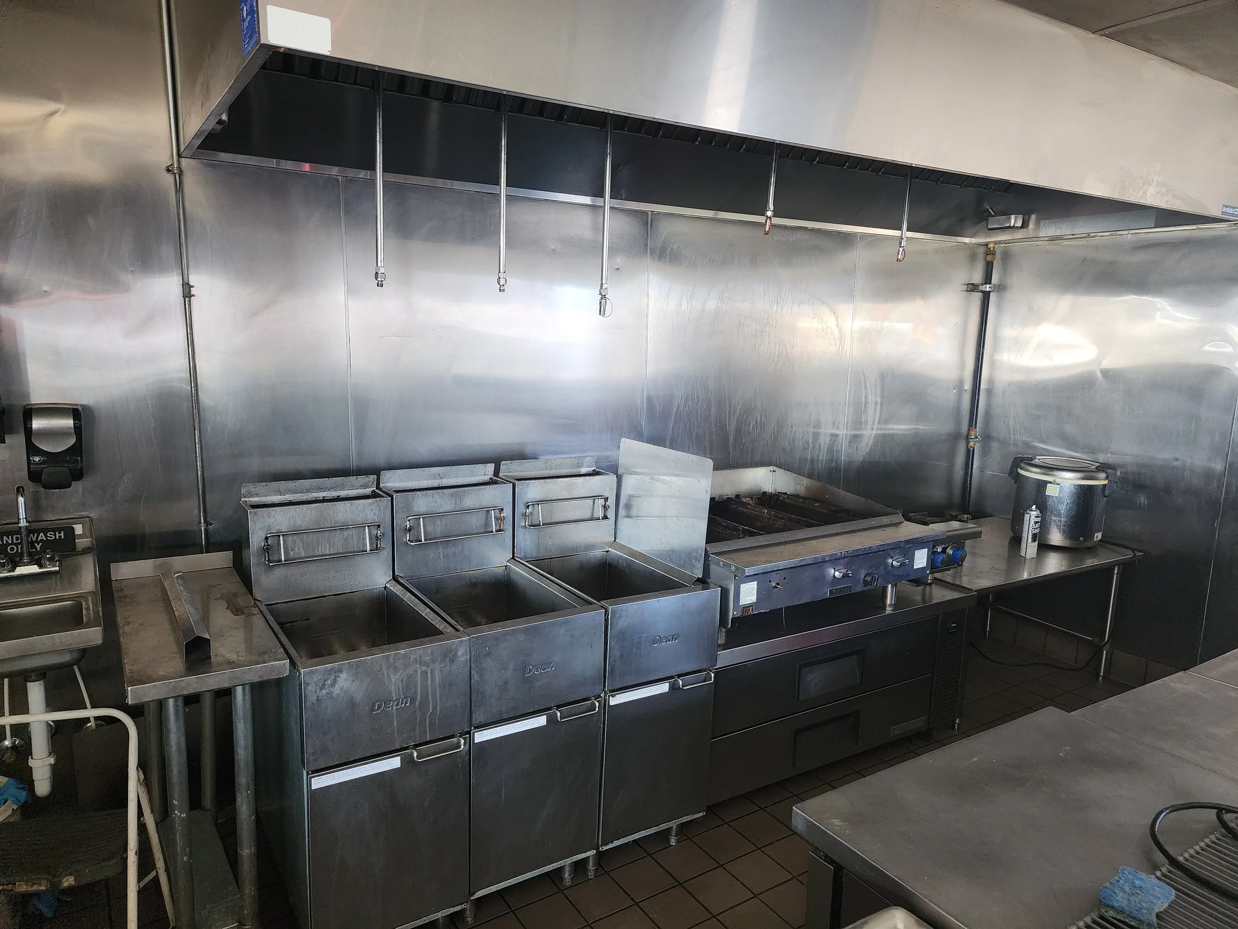 Commercial kitchen with stainless steel appliances, including fryers, stove, and preparation tables.