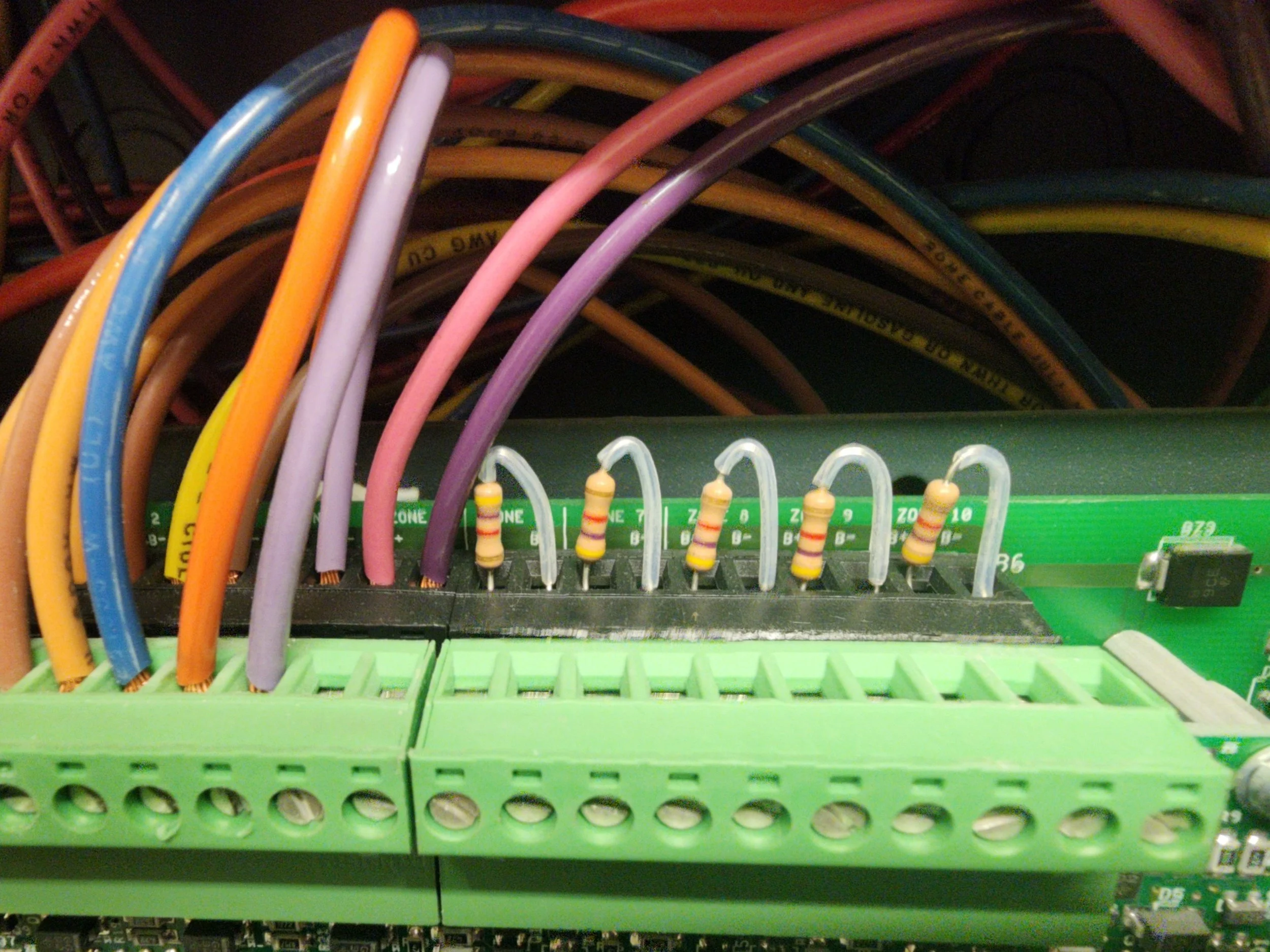 An electronic circuit board with multiple colorful wires connected to it and resistors mounted on the board.