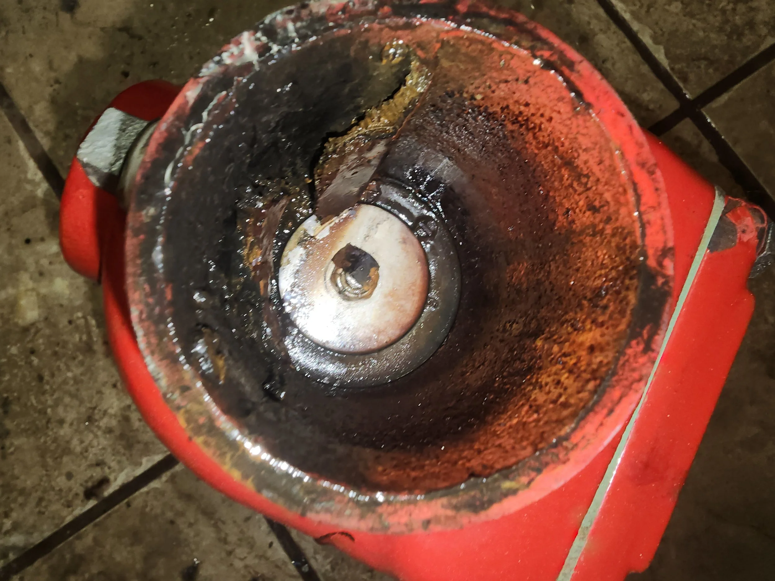 Inside of a rusty, cylindrical metal grinder, showing signs of wear and leftover coffee grounds, mounted on a tiled countertop.
