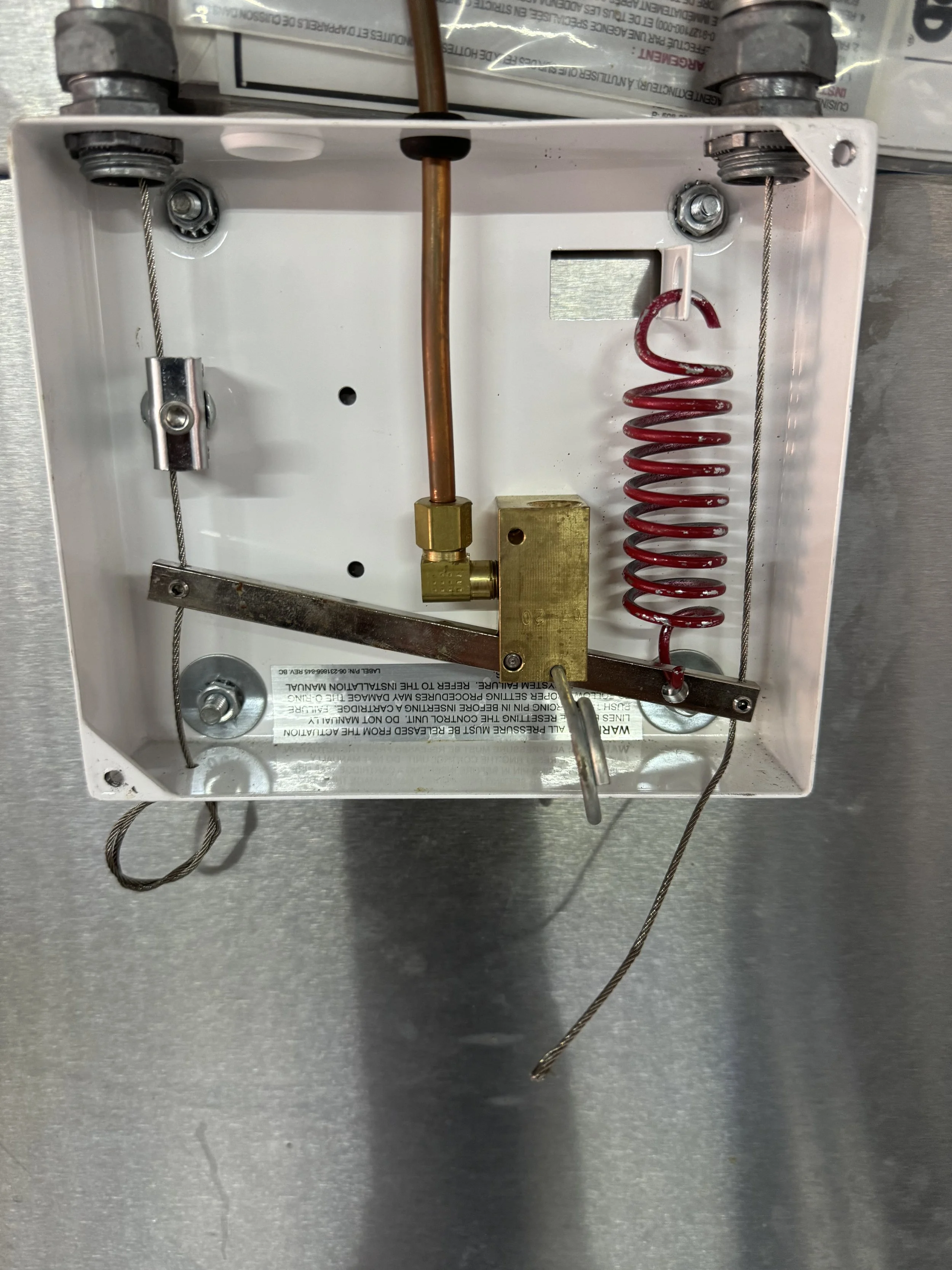 Interior of a small electrical or mechanical device with wires, a copper pipe, a red coil spring, and metal components mounted inside a white box.