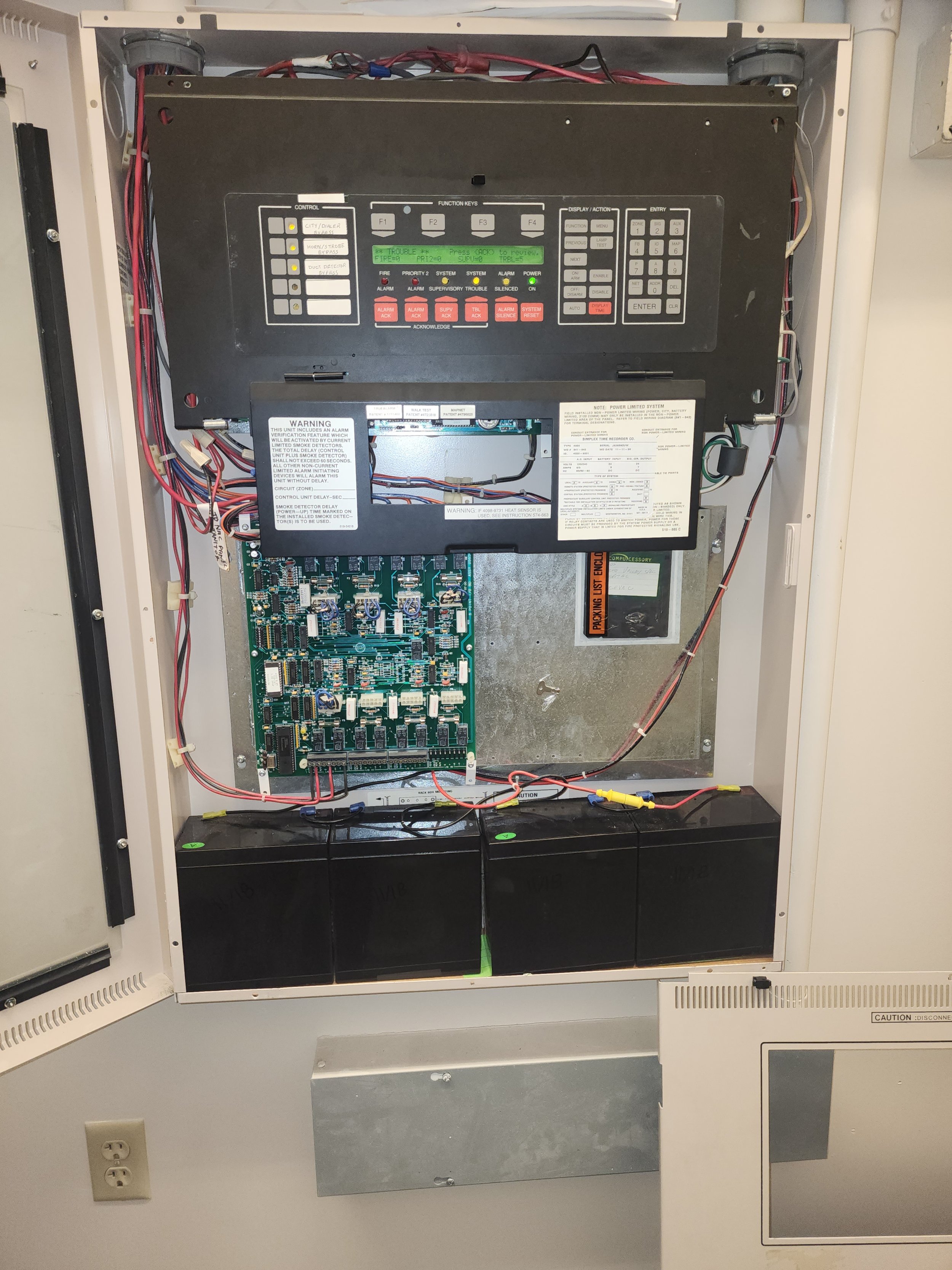 Internal components of a building fire alarm control panel, including circuit boards, wiring, and battery backups.