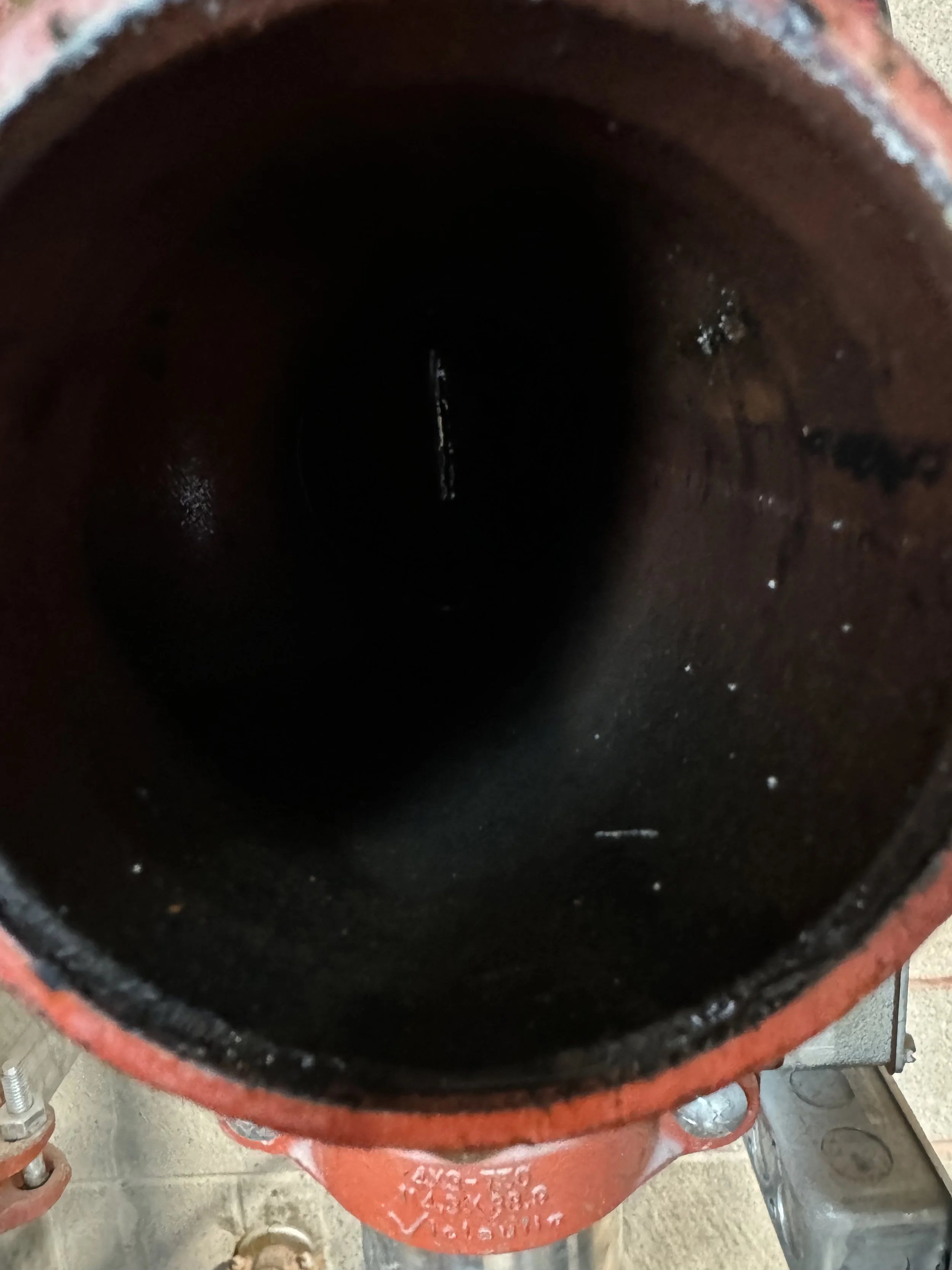 Close-up of the interior of a large red pipe or cylinder, showing dark, hollow inside with some reflections and minor debris, possibly part of industrial equipment or machinery.