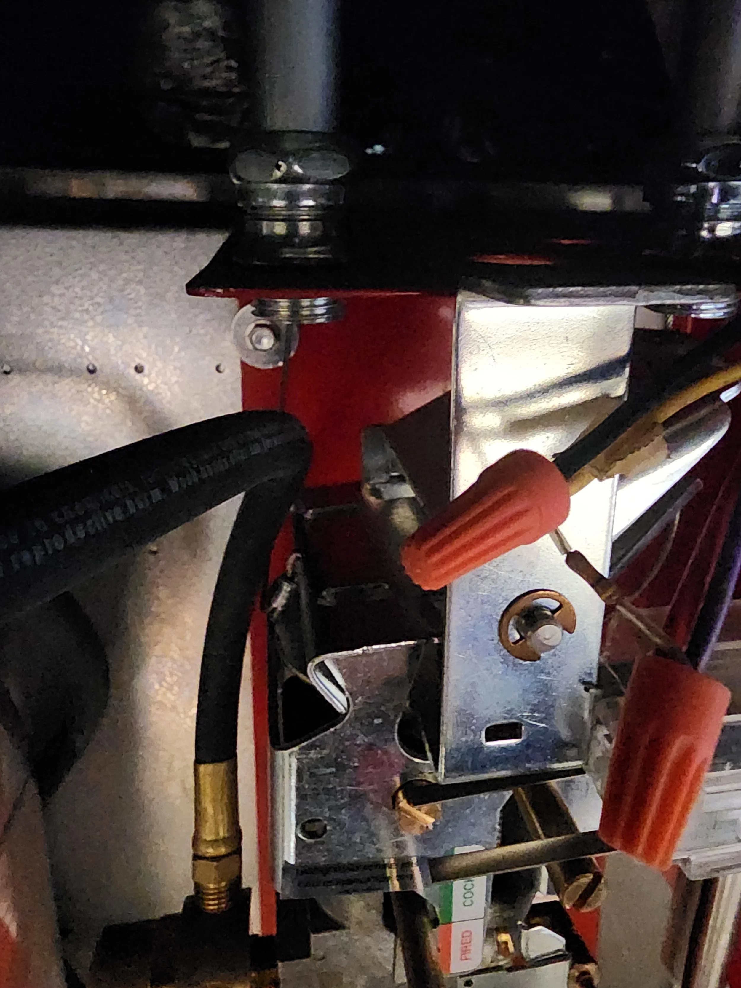 Close-up of machinery with metal, black hoses, and orange knob handles, possibly part of a hydraulic or fuel system.