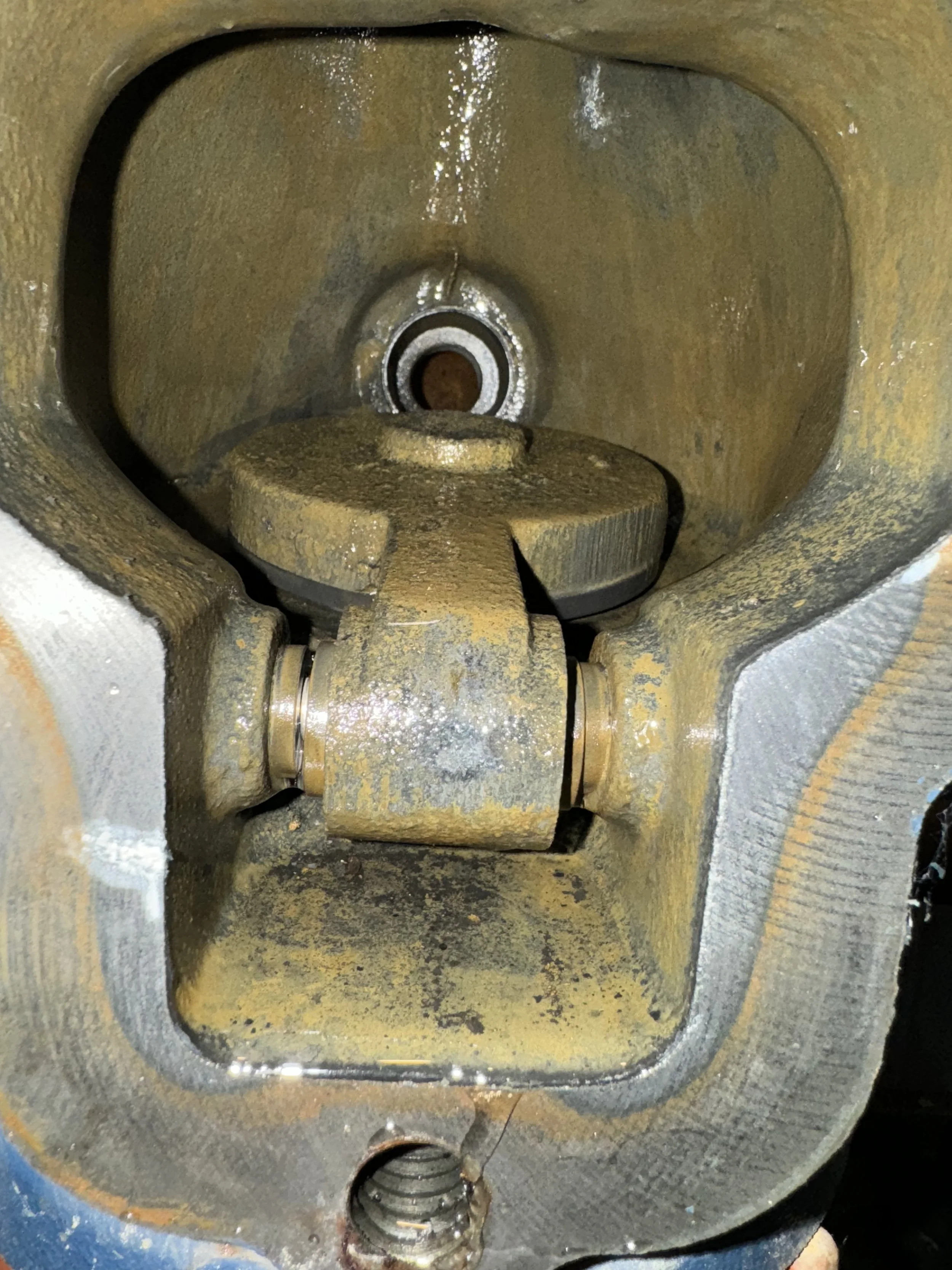 Close-up of a worn, metallic internal part of a mechanical device or engine, showing a central bearing, a pivot point, and a spring at the bottom.