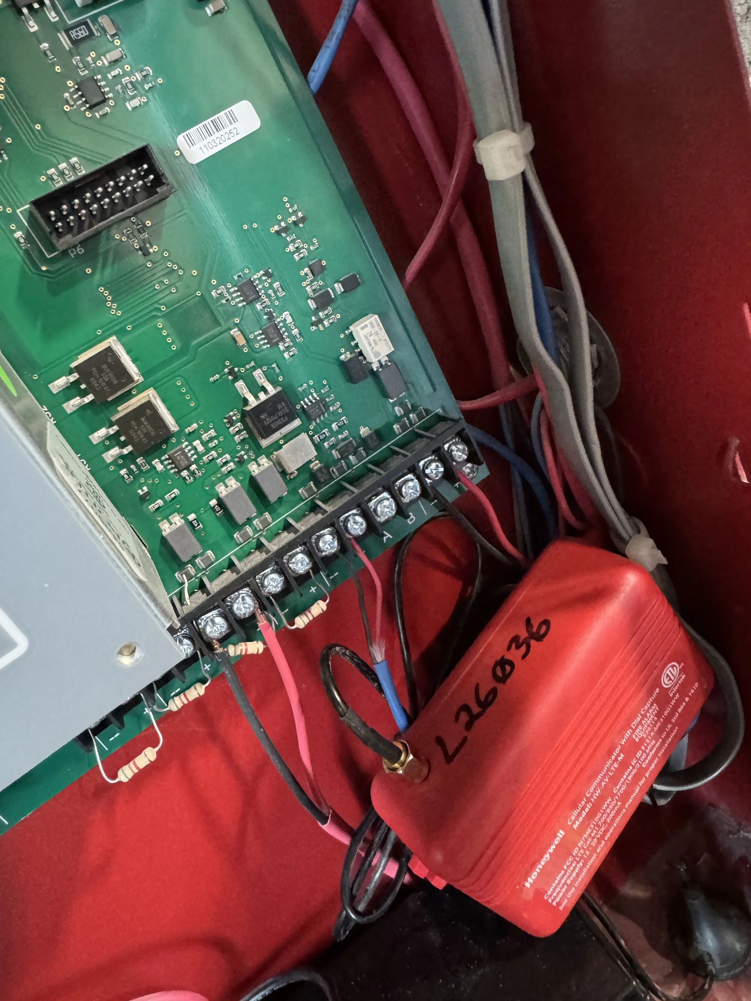 Close-up of an electronic circuit board with various components and wires connected to a red device labeled 'L26036'.