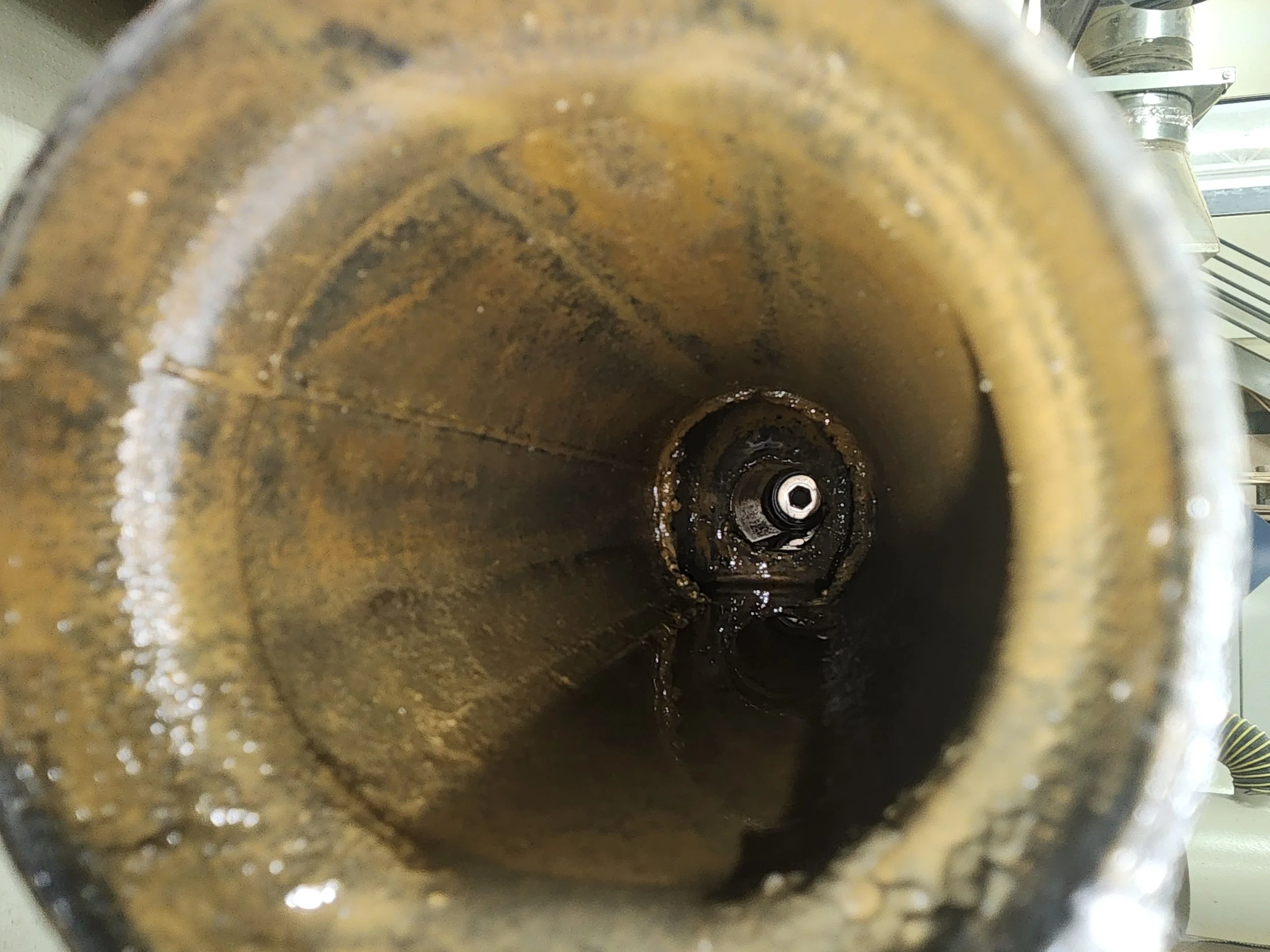 Close-up view of an empty, dirty metal pipe with some water and rust inside, looking toward the other end.