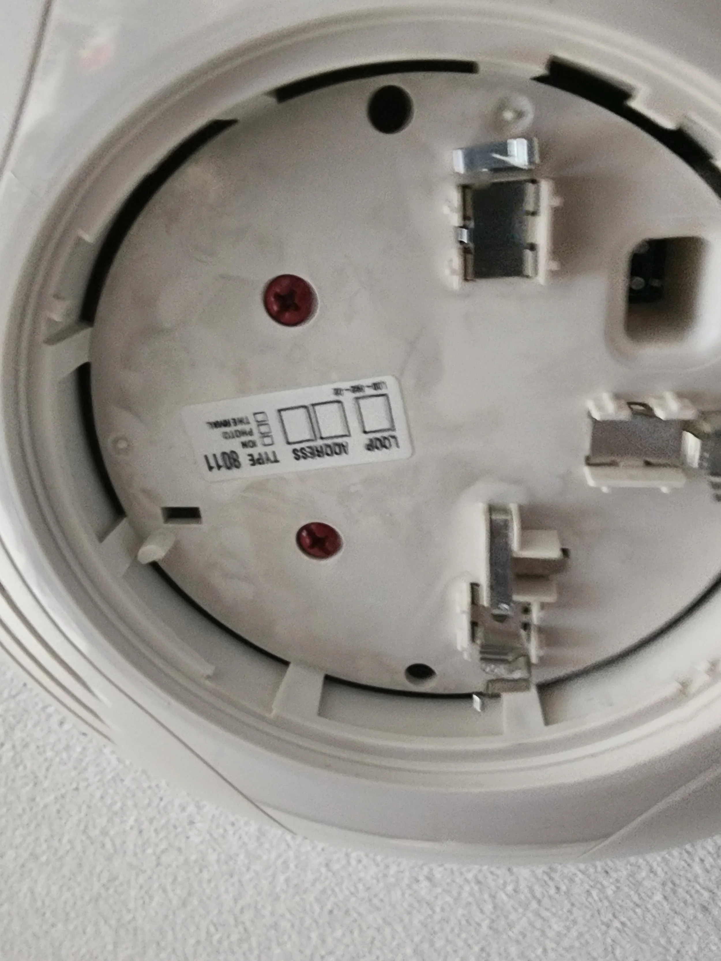 Close-up of the back of a smoke detector, showing electrical connectors and mounting screws.