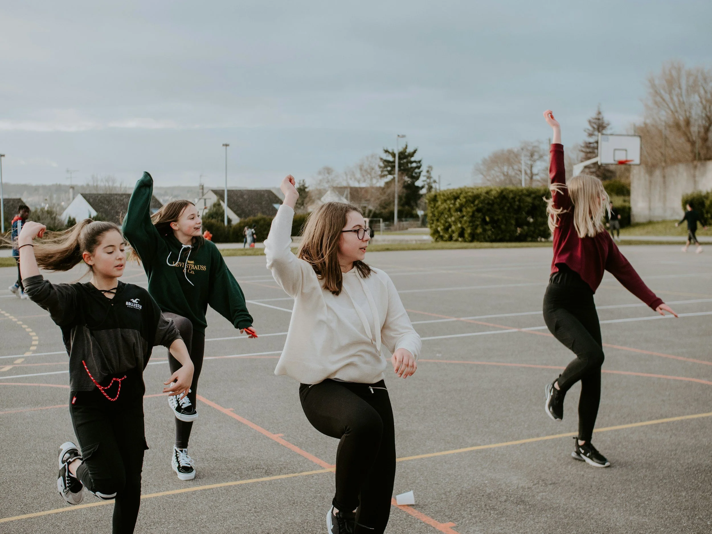 Group of young girls and women participating in a jump rope activity on an outdoor basketball court, with mountains and houses in the background.