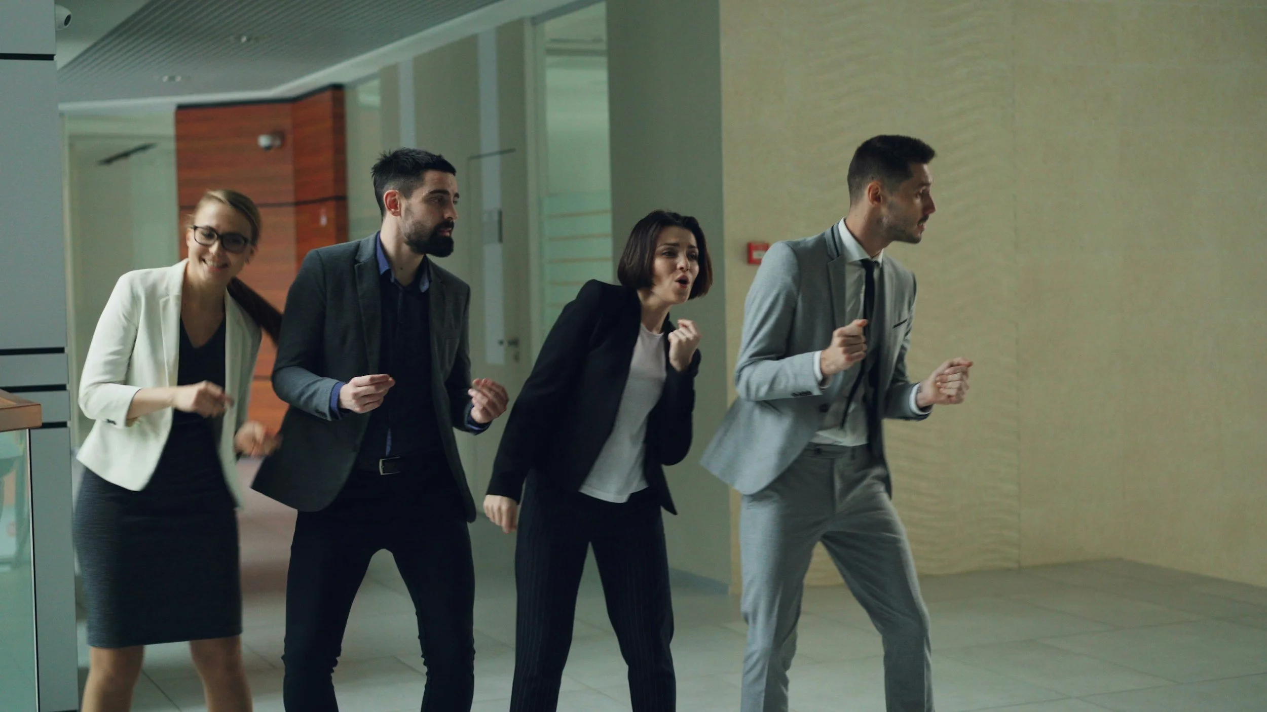 Four business professionals, two men and two women, walking through an office hallway and talking.