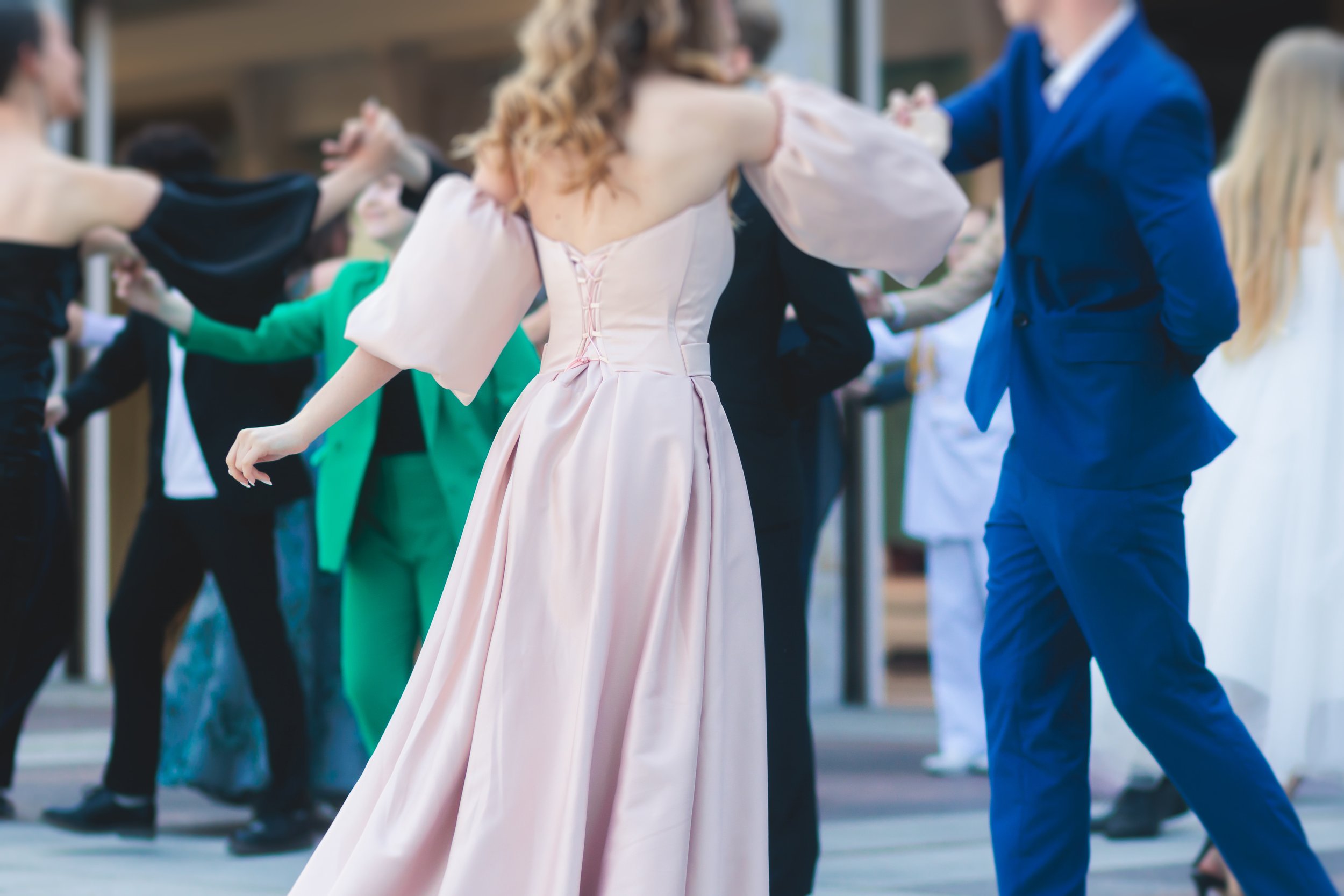 People in formal attire dancing at a celebration, with women in elegant dresses and men in suits.
