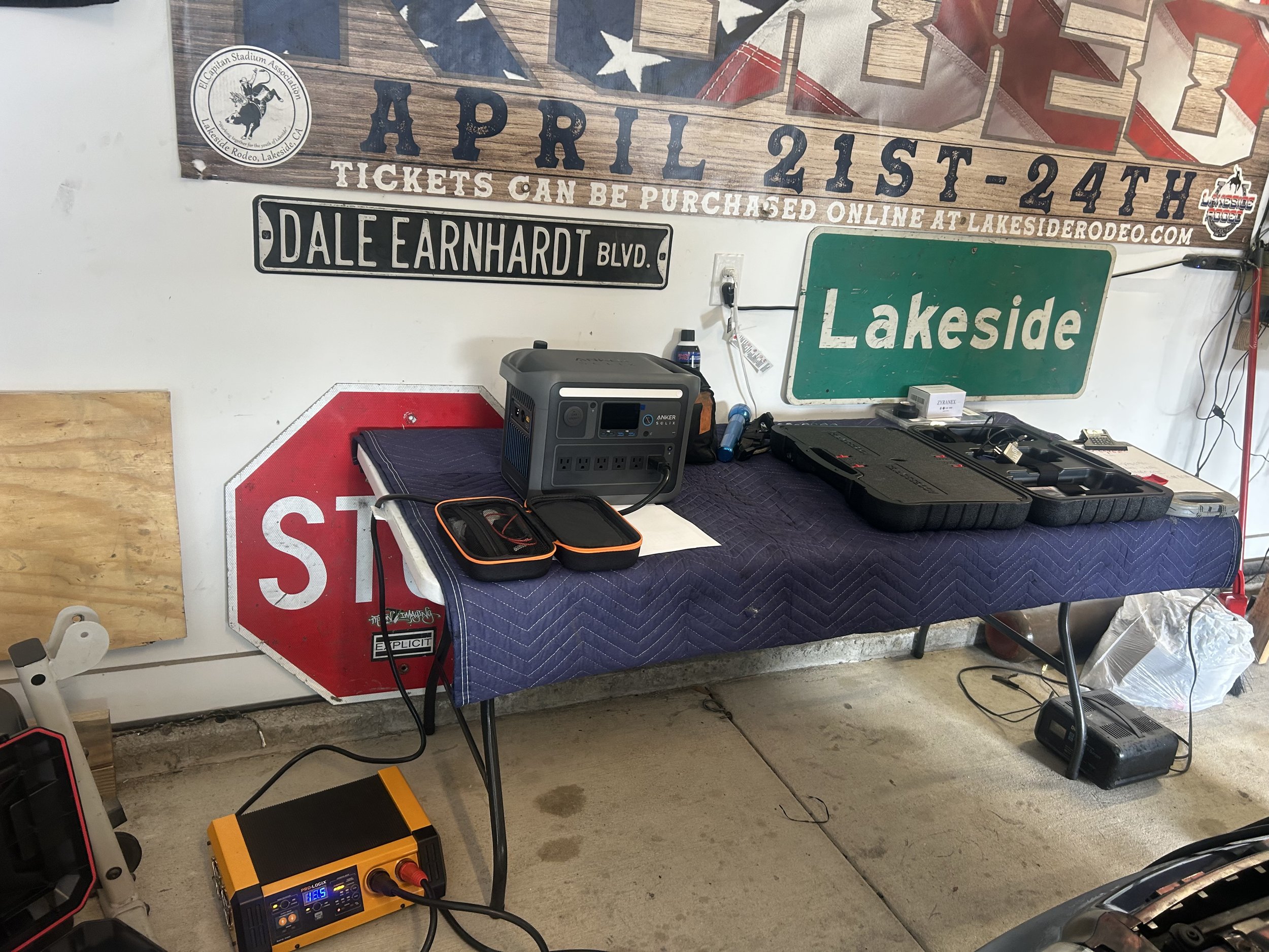 A table with electronic devices and tools in front of a white wall decorated with various street signs and banners, including one that reads 'April 21st-24th' and another labeled 'Lakeside'.