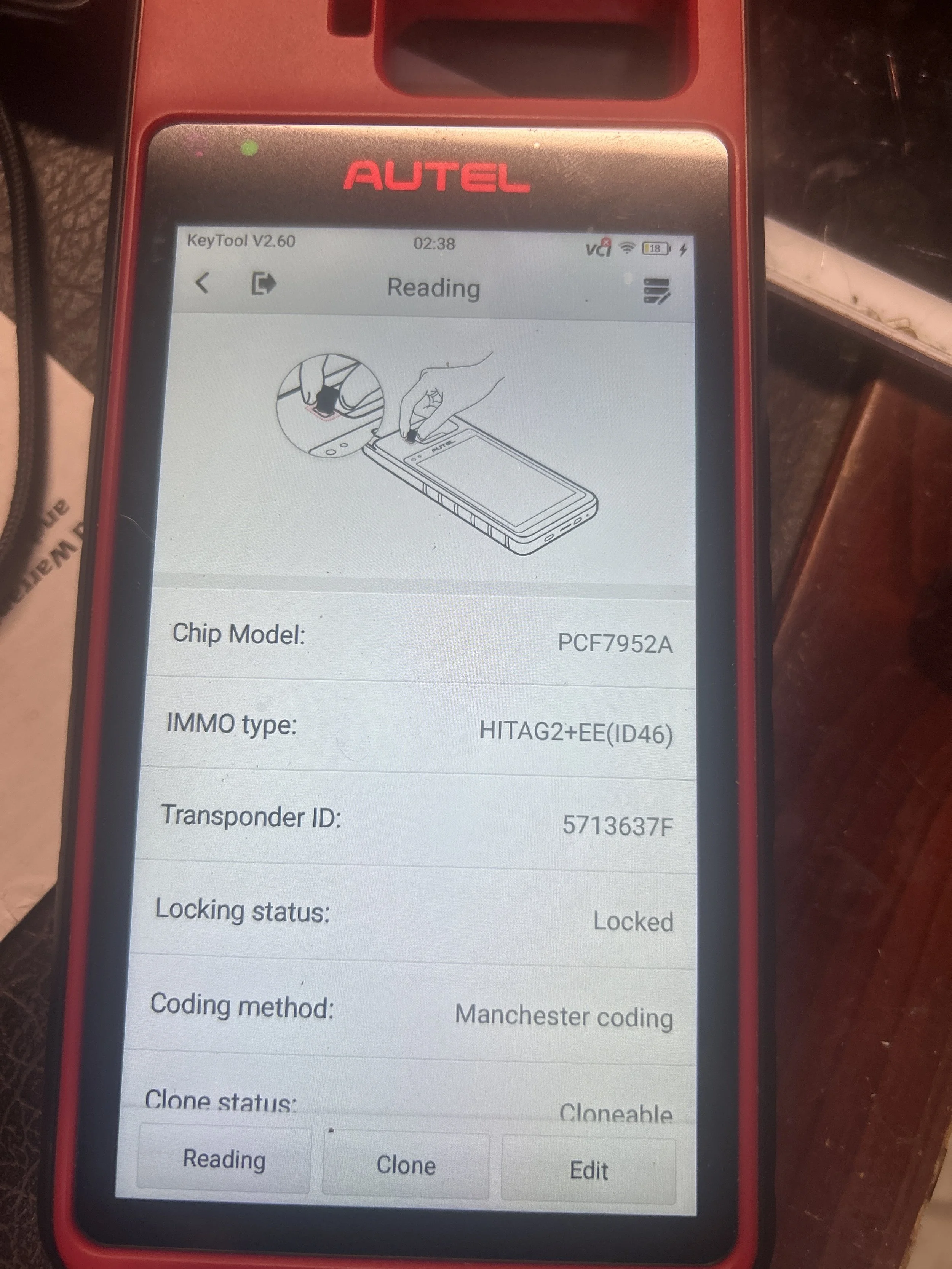 Close-up of a smartphone screen displaying information about a chip, including chip model, IMMO type, transponder ID, locking status, coding method, and clone status. The phone is in an AUTEL device.