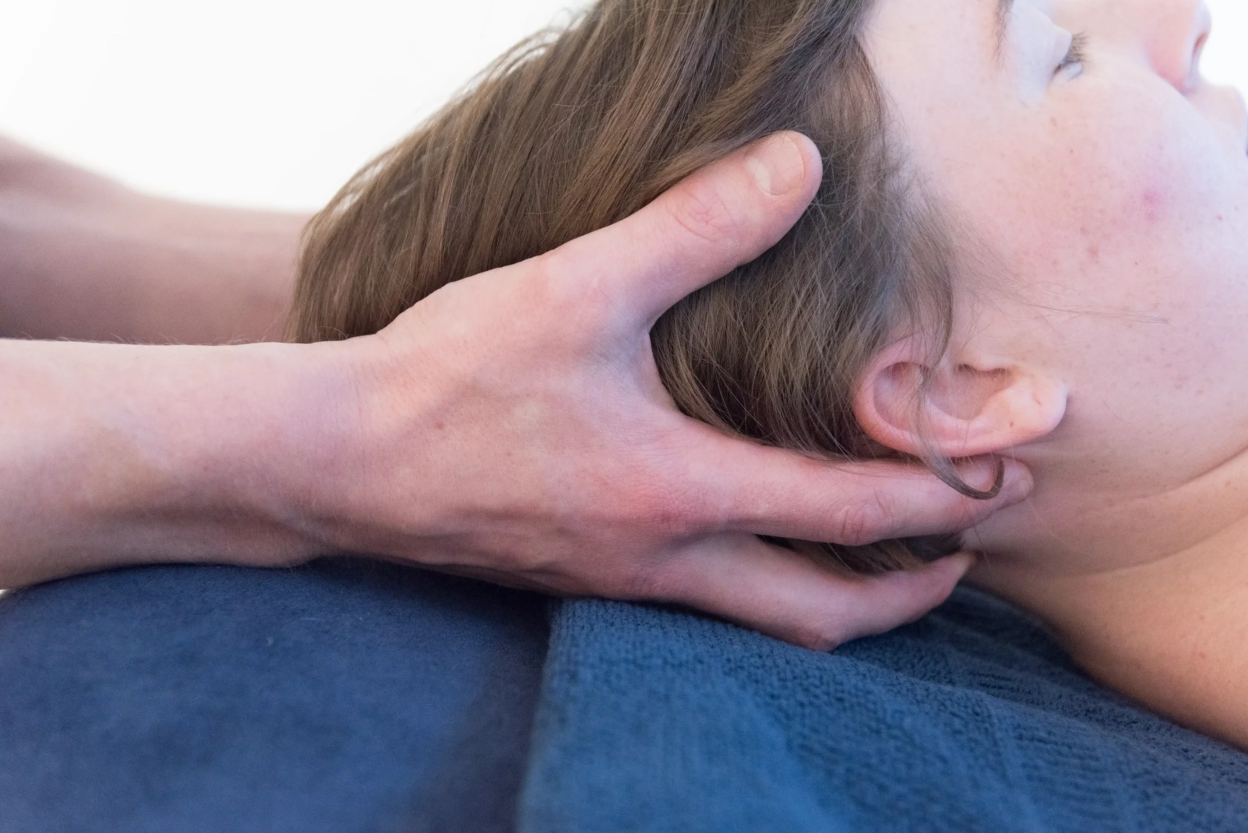 Close-up van een persoon die een nekbehandeling krijgt van de osteopaat, met handen die de nek vasthouden en ontspannen in de suboccipitale regio.