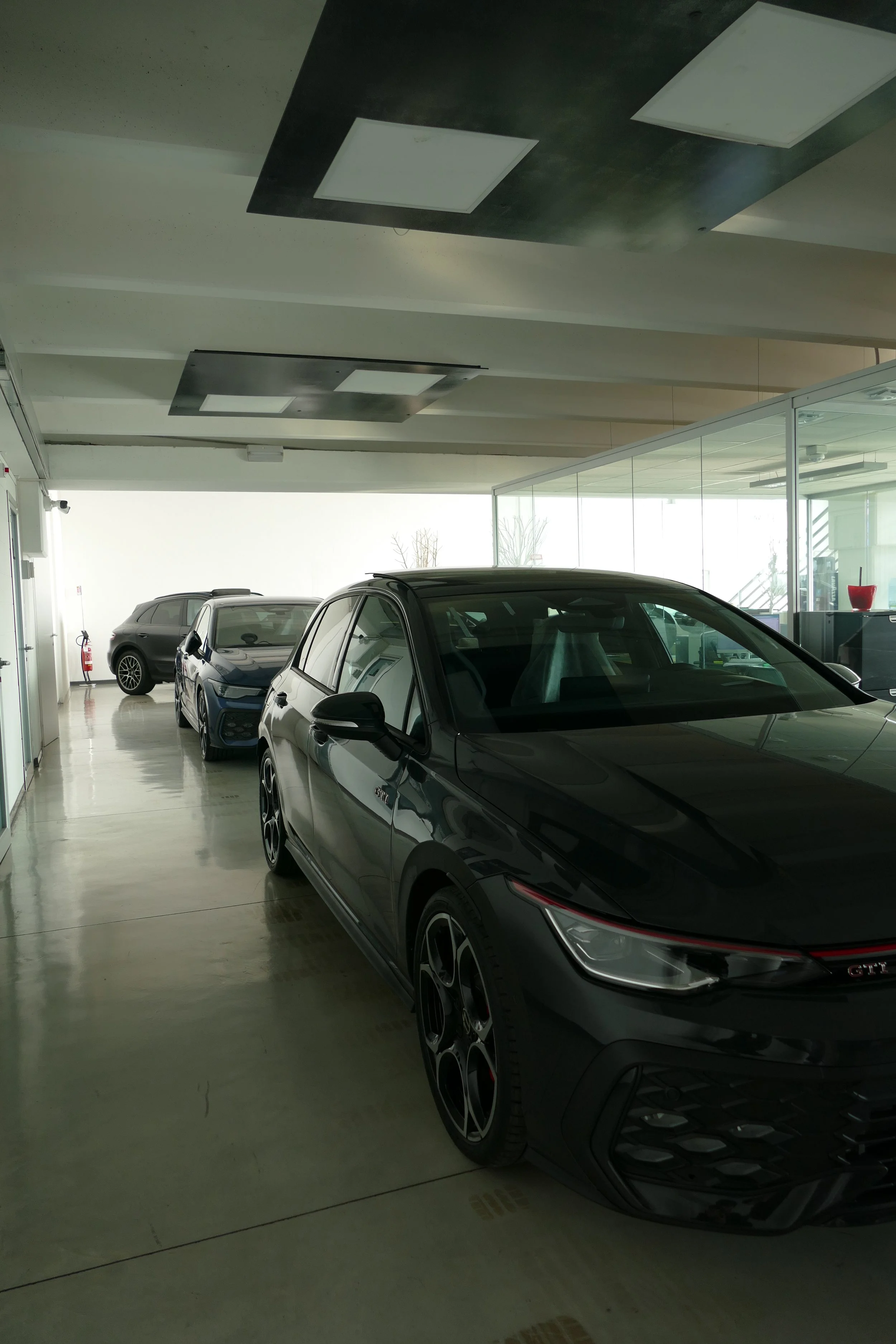 Interno di una concessionaria di auto, con tre auto parcheggiate, una nera nuove, e pareti di vetro, ambiente luminoso.