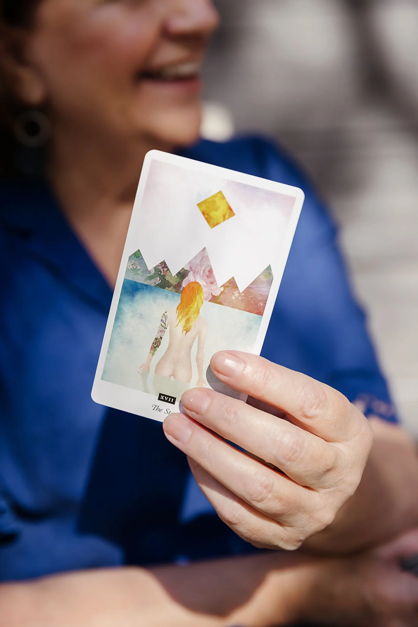 A woman holding a tarot card with a colorful illustration of a woman with long blonde hair and mountains in the background. El Chambers and Nicole Perry offering women's spiritual retreats and empowerment coaching in Victoria.