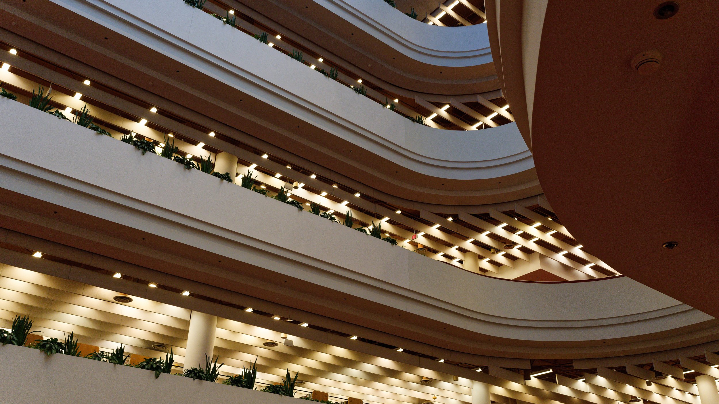 Interior view of a multi-story parking garage with curved, illuminated railings and green plants on each level.
