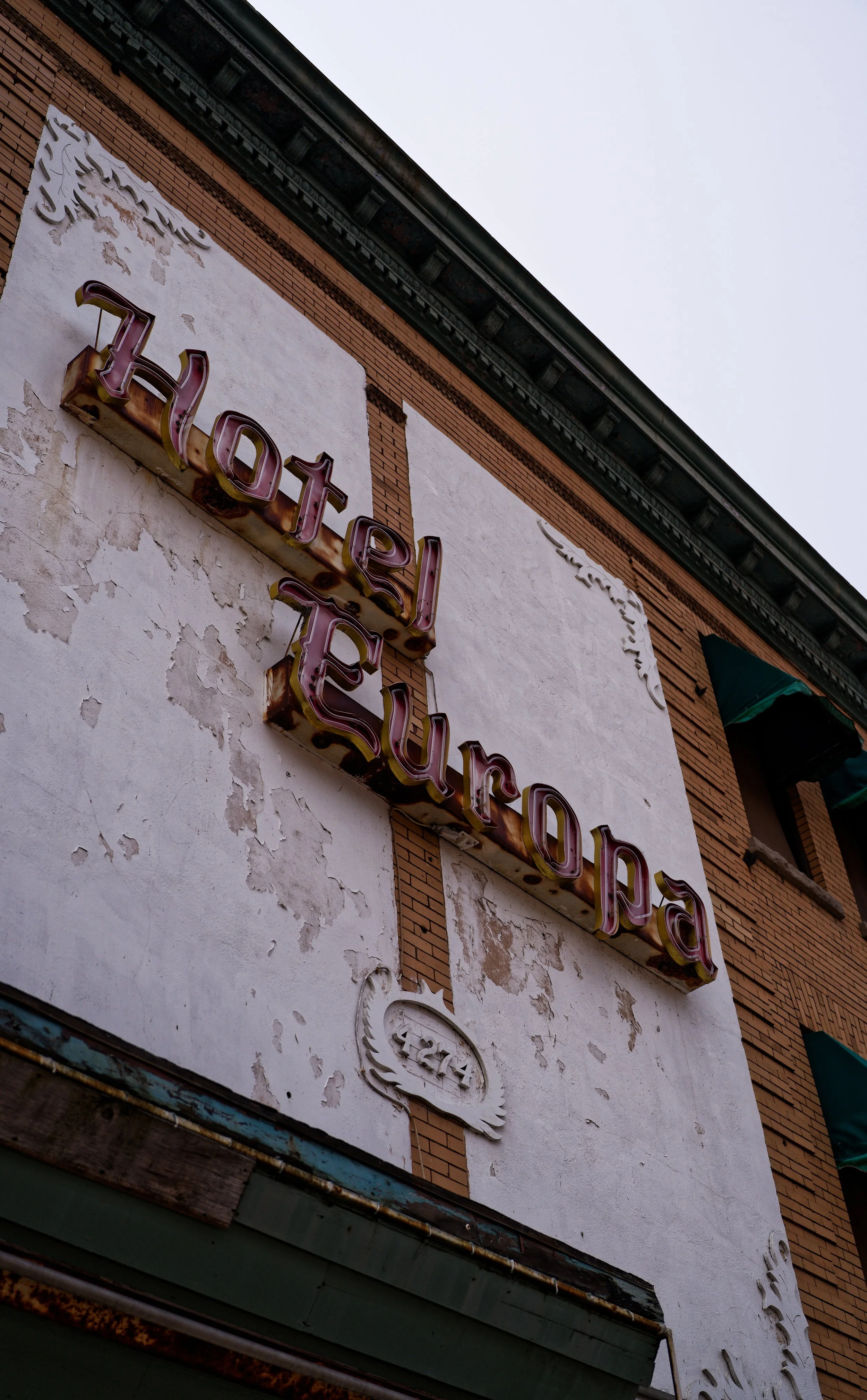 Close-up of a vintage neon sign that reads 'hotel europa' on a weathered building with peeling paint and brick accents.