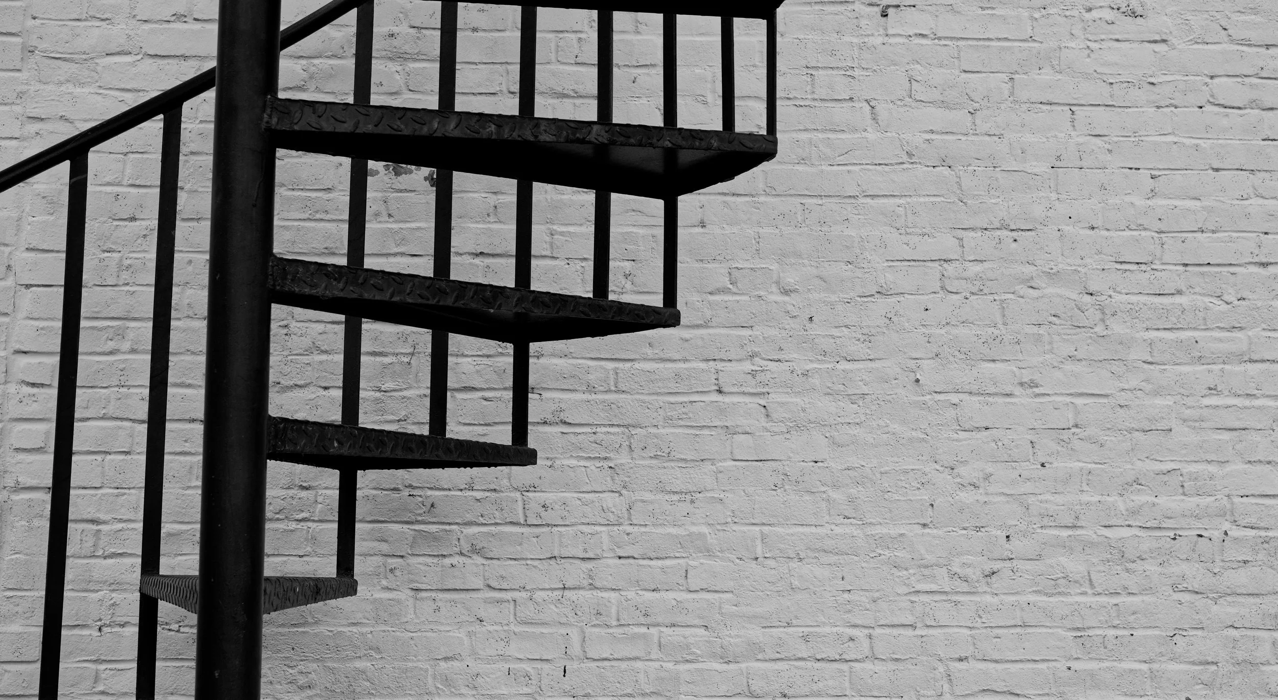 Close-up of a black metal spiral staircase against a white brick wall.