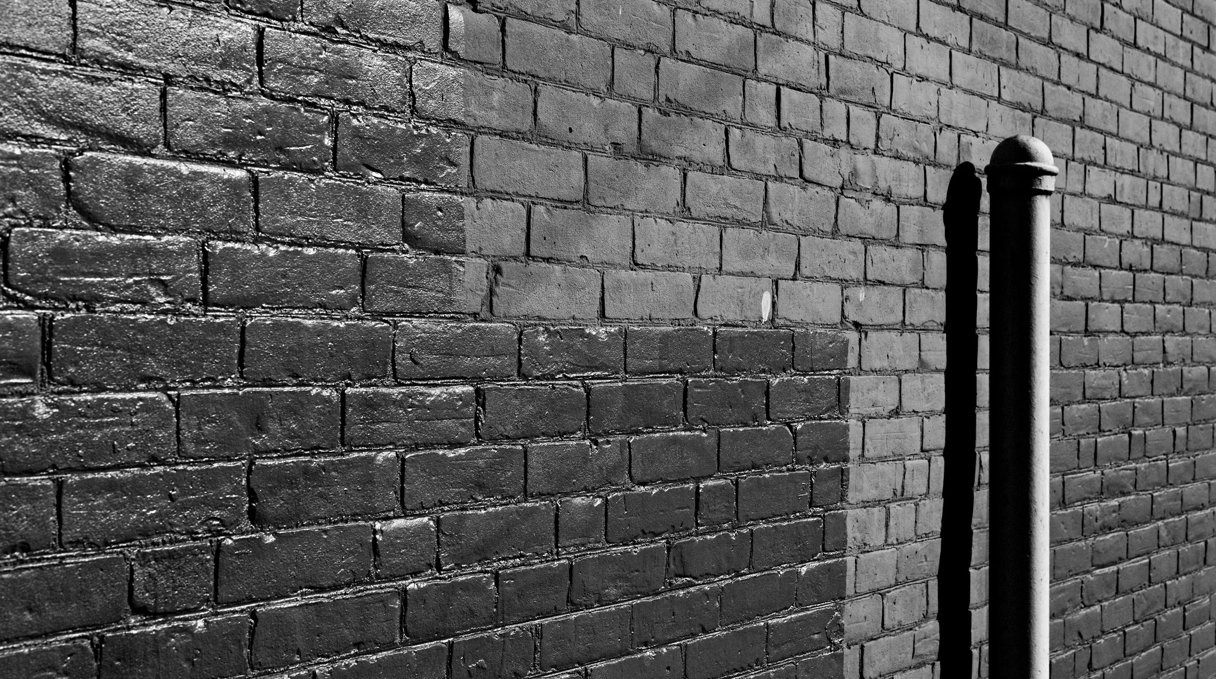 A brick wall with a metal pipe casting a shadow on it.