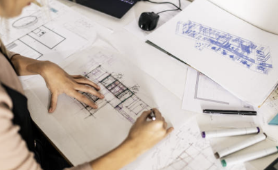 Architect working on blueprints and architectural drawings with pens and sketches on a desk.