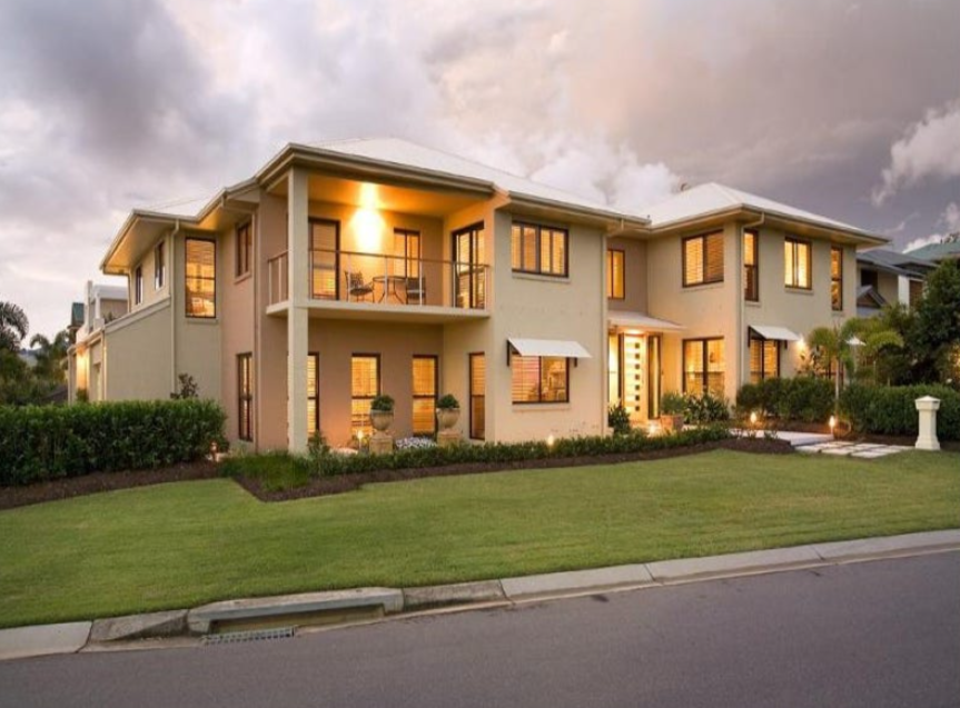 A modern two-story house with large windows, a small balcony, and well-maintained front yard, illuminated at dusk. Custom Home.