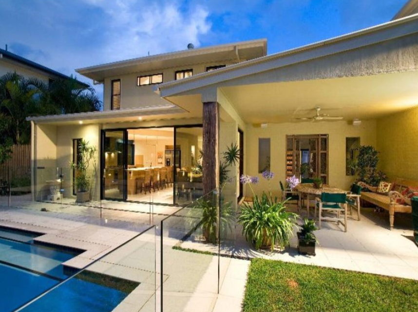 Modern house with outdoor patio, glass fencing, swimming pool, and garden at dusk.